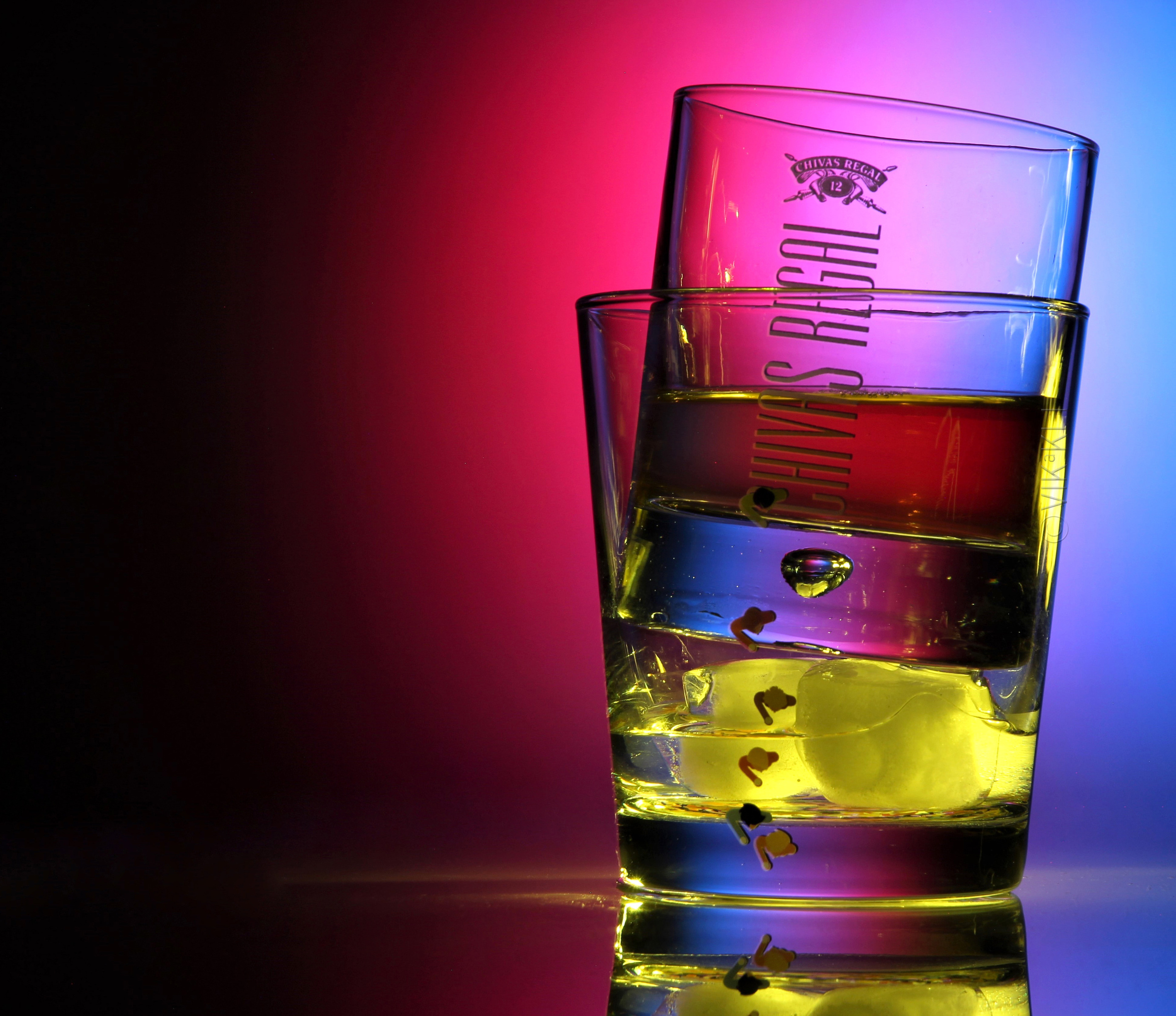 Стеклянные стаканы Chivas Regal с виски на розово-голубом фоне. Предметное фото.