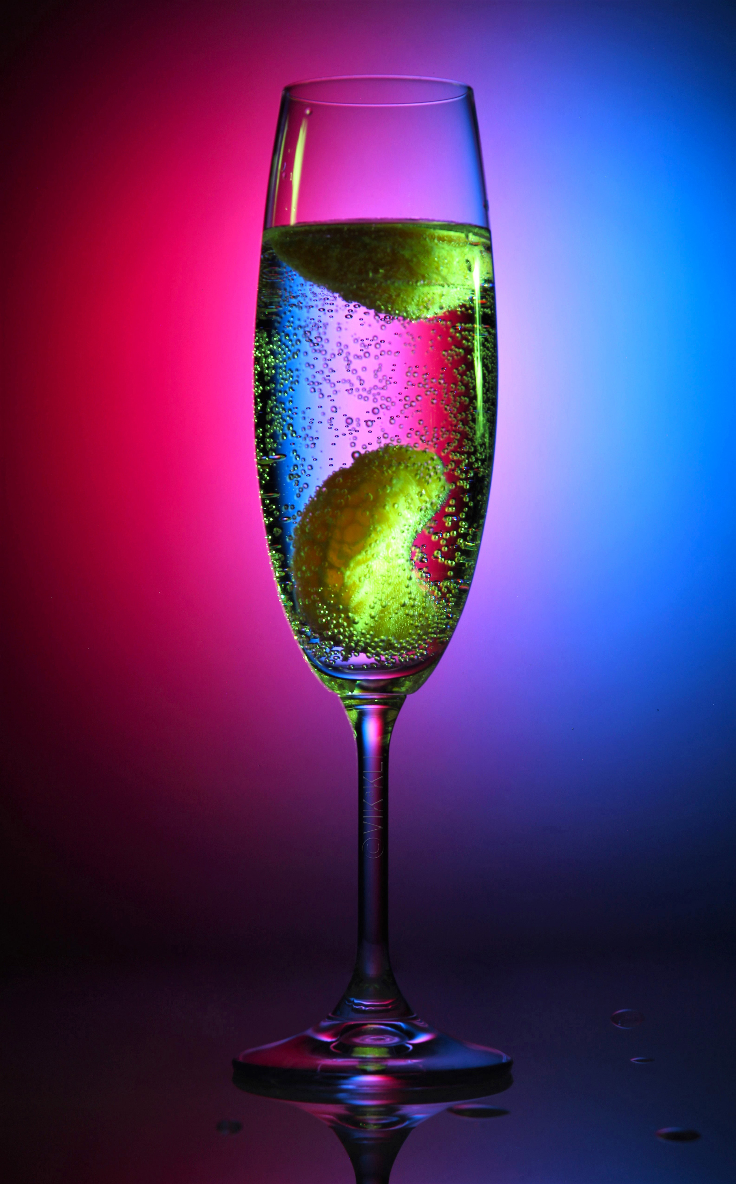 Стеклянный бокал с шампанским на розово-голубом фоне. Предметное фото.