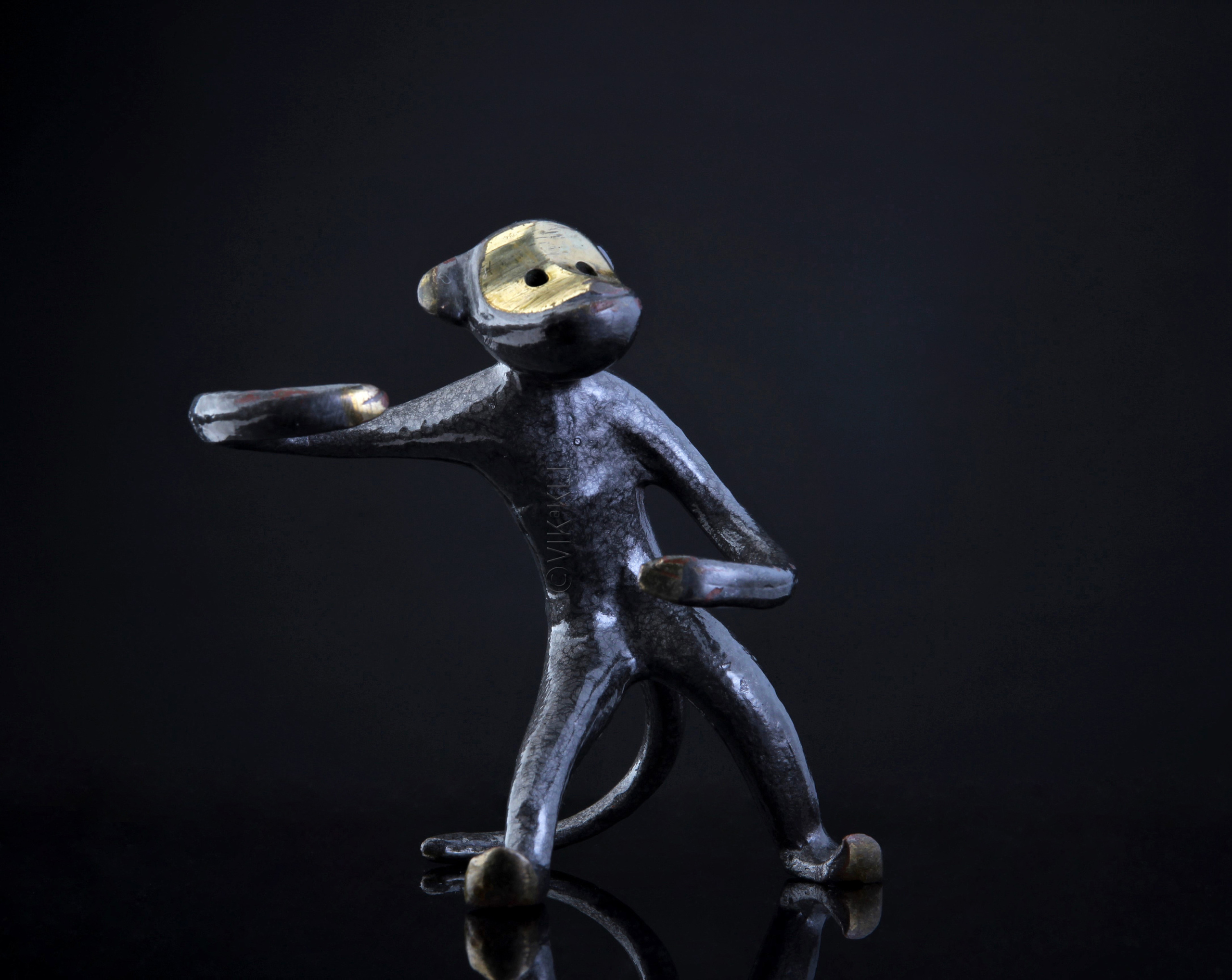 Бронзовая статуэтка обезьяны на тёмном фоне. Предметное фото.