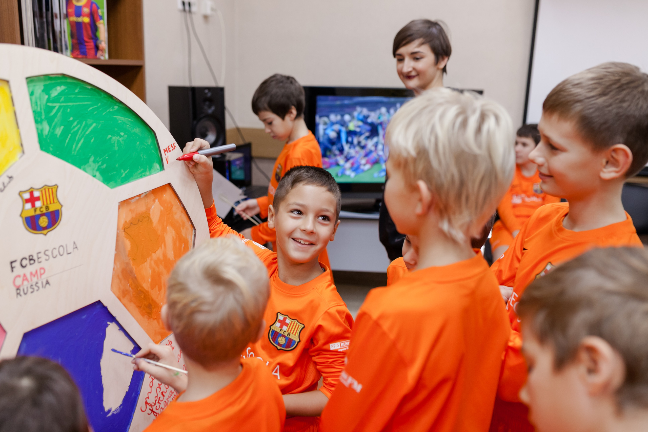 Ученики футбольной школы в оранжевых футболках рисуют на большом мяче