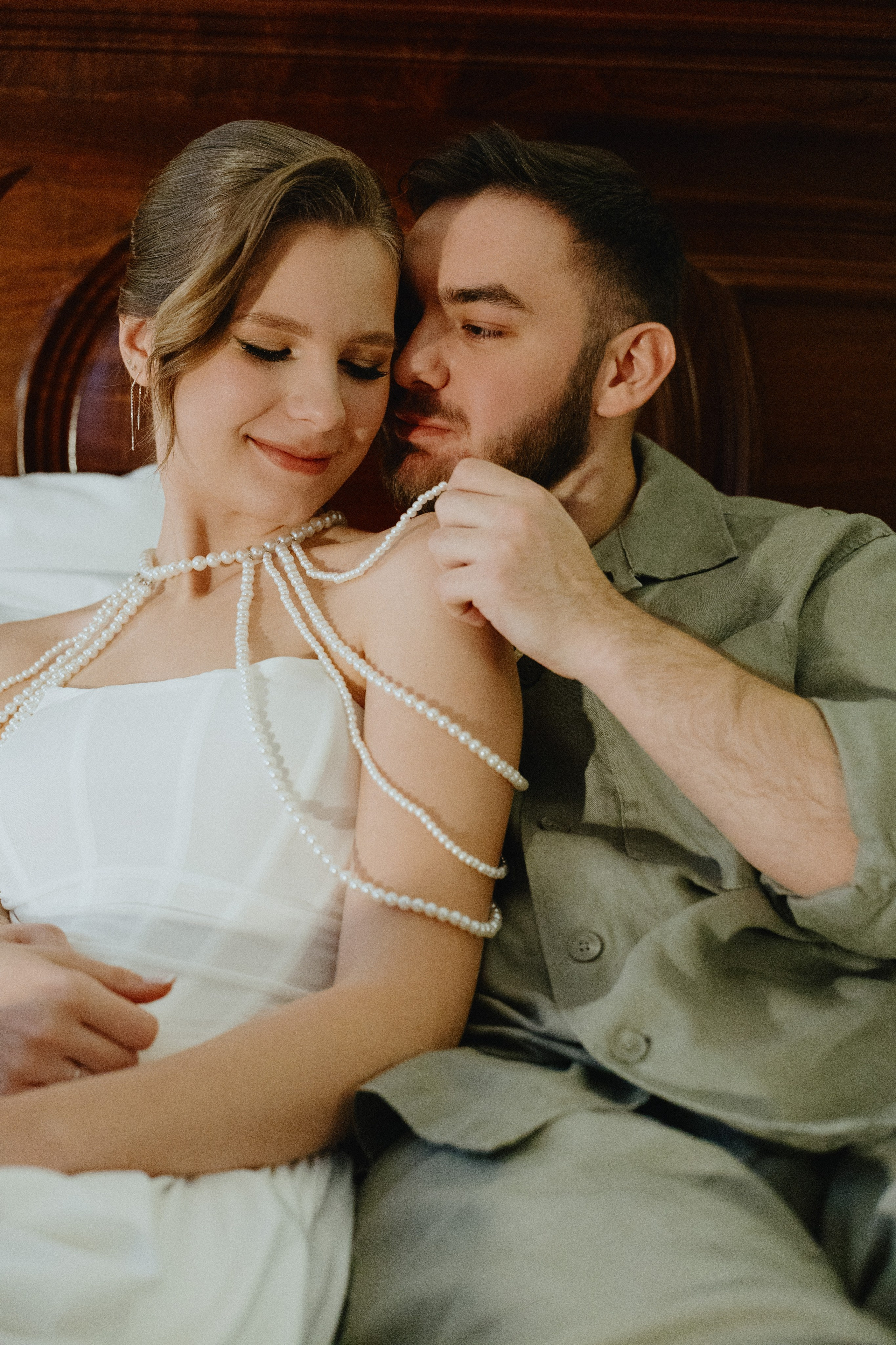 Жених и невеста нежно обнимаются, сидя на кровати.