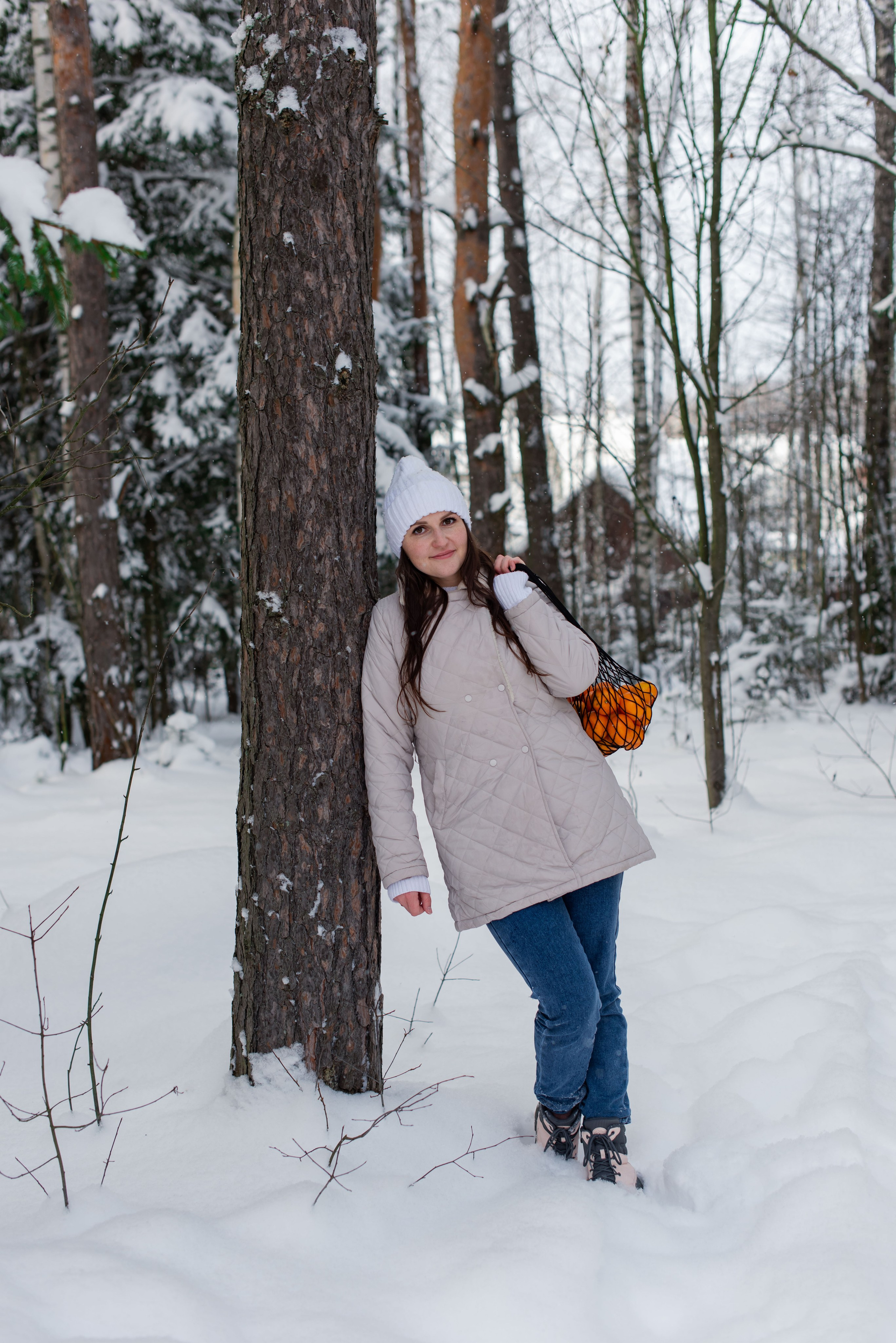 Зимняя сцена: девушка держит сетку с цитрусовыми, вокруг — лесная местность.
