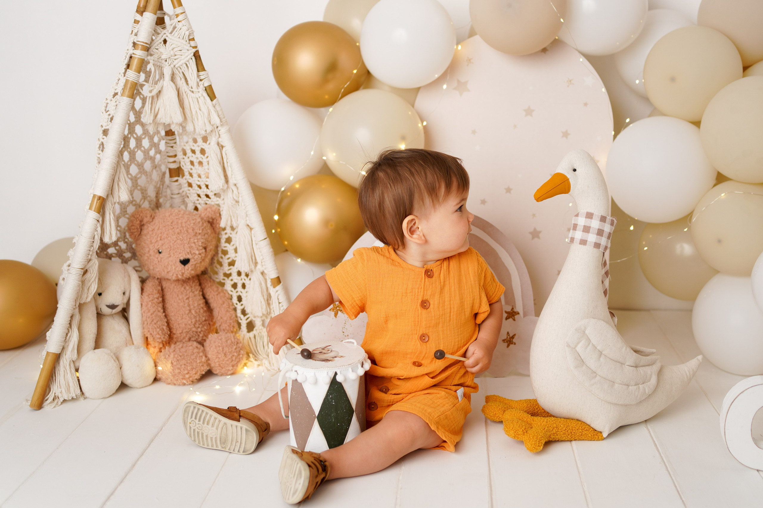 Малыш сидит на полу в окружении игрушечного гуся, мишки , зайки.