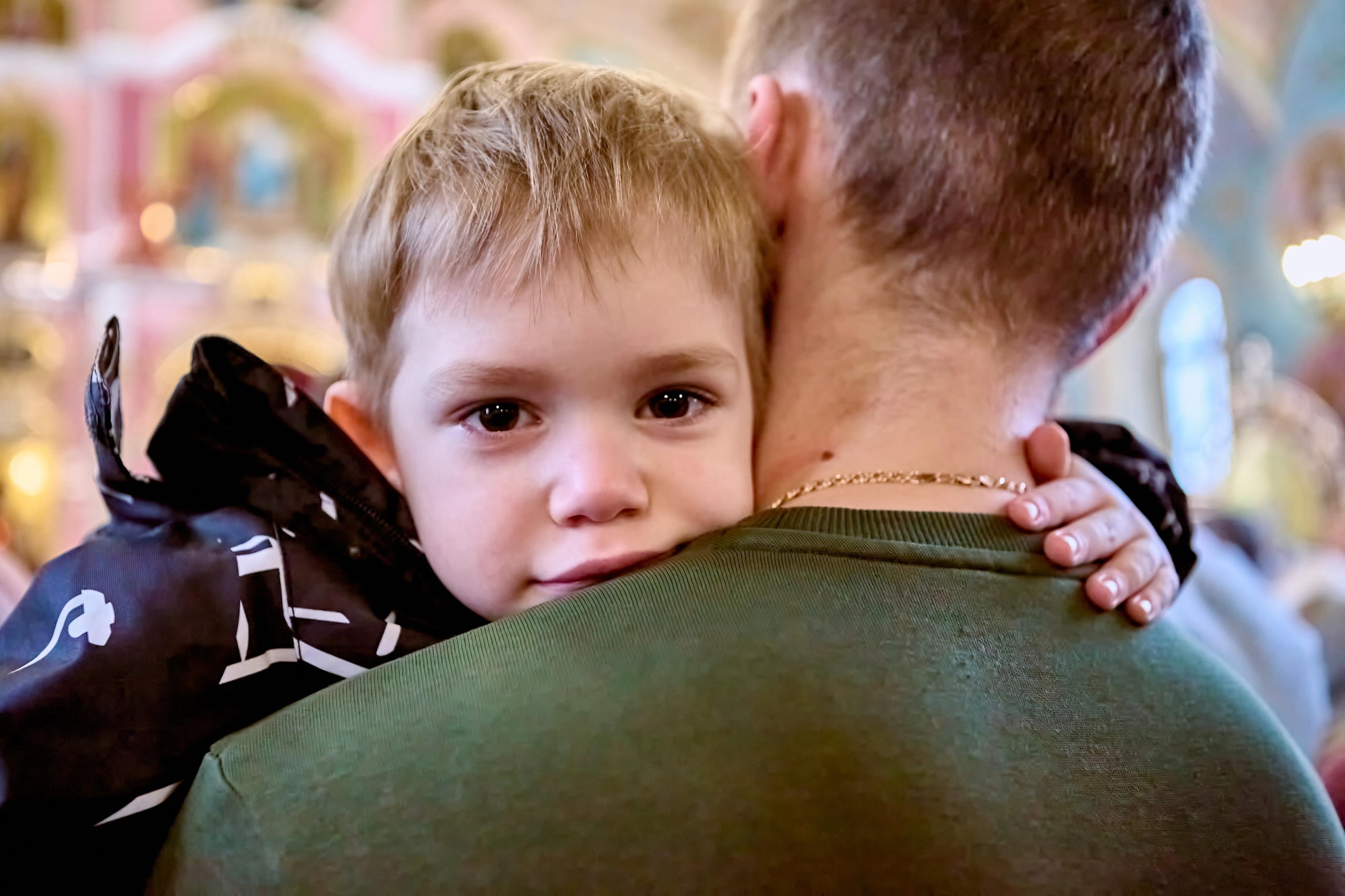 Малышка на руках у папы смотрит за спину и держится за шею 