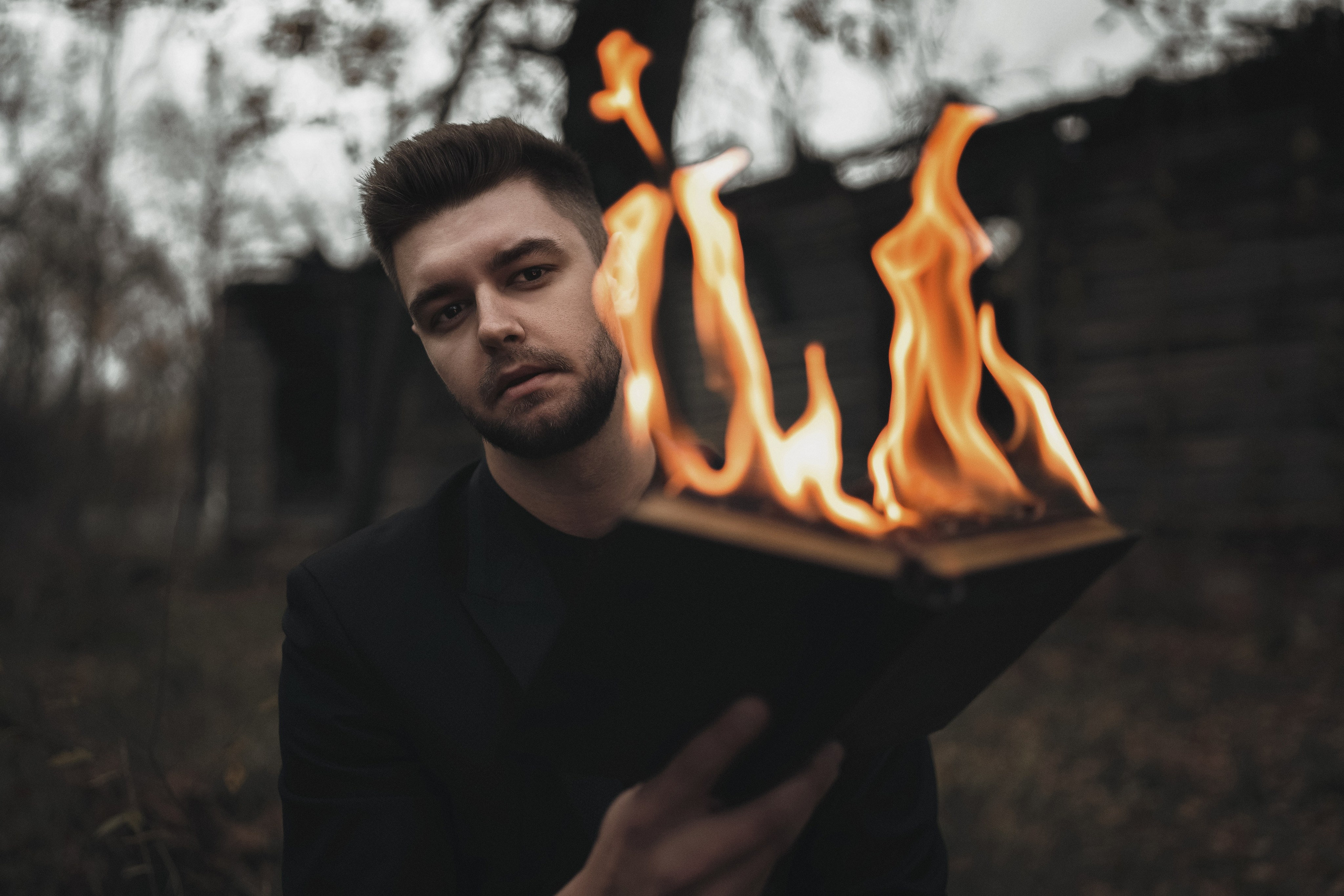 Парень в строгом черном костюме держит горящую книгу. Фотография Романа Яковенко