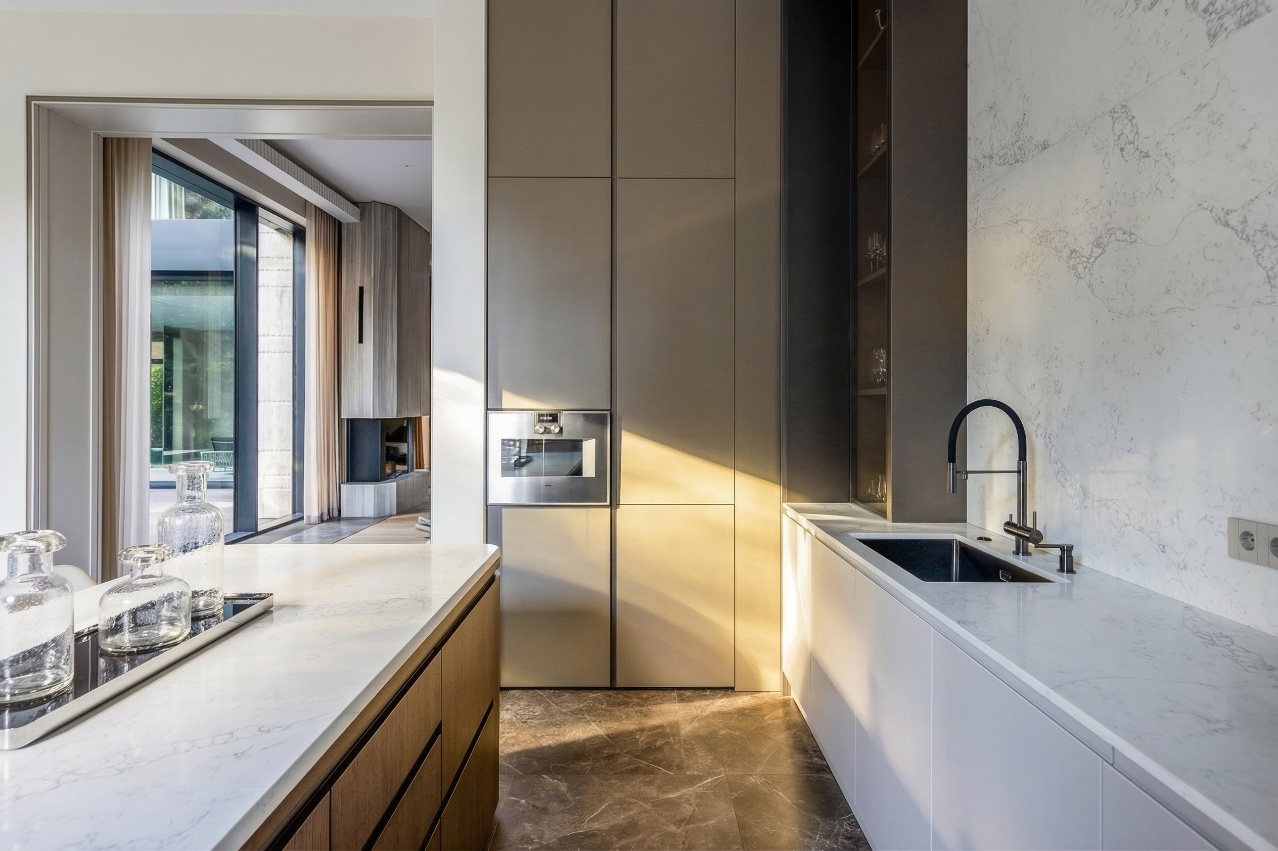 Вид на рабочую зону кухни с мраморной столешницей и встроенной техникой, анфиладная перспектива в сторону гостиной, проект Валерии Котович, дом 1240 м² в Подмосковье.