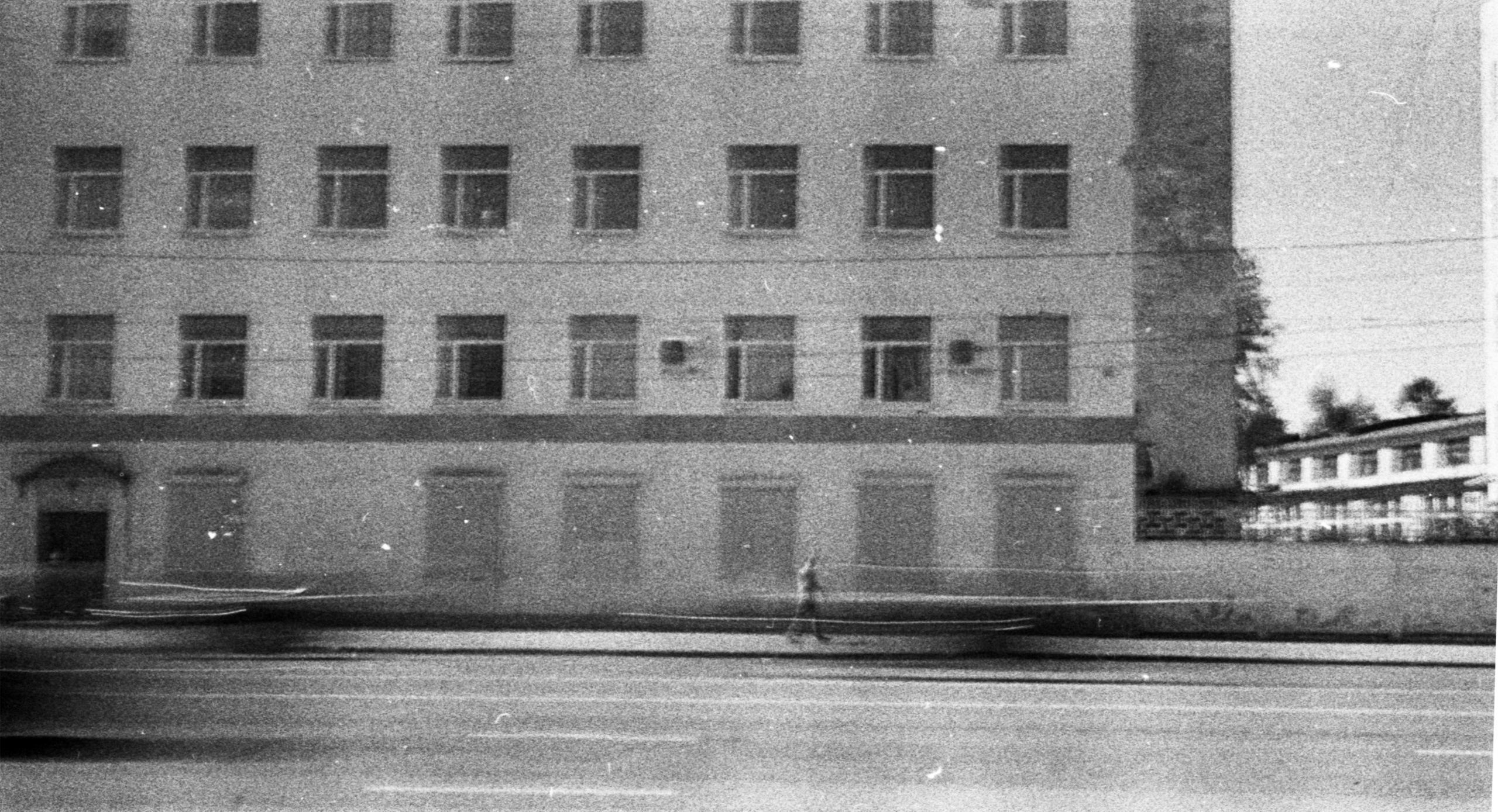 Монохромная фотография фасада здания и улицы с эффектом длинной выдержки, смазанным движением и выцветшими тонами.