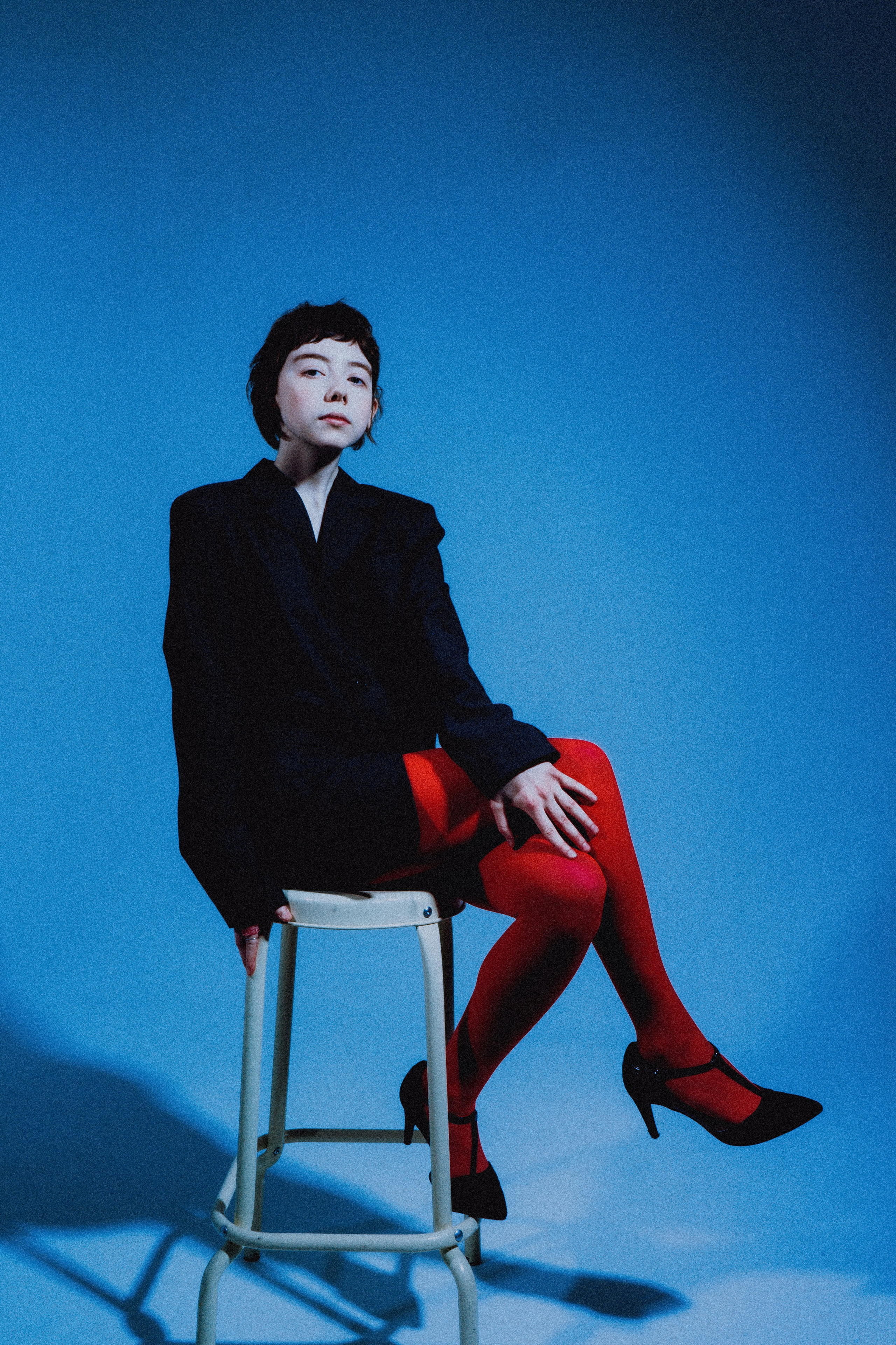Девушка сидит на стуле в красных колготках и на синем фоне 