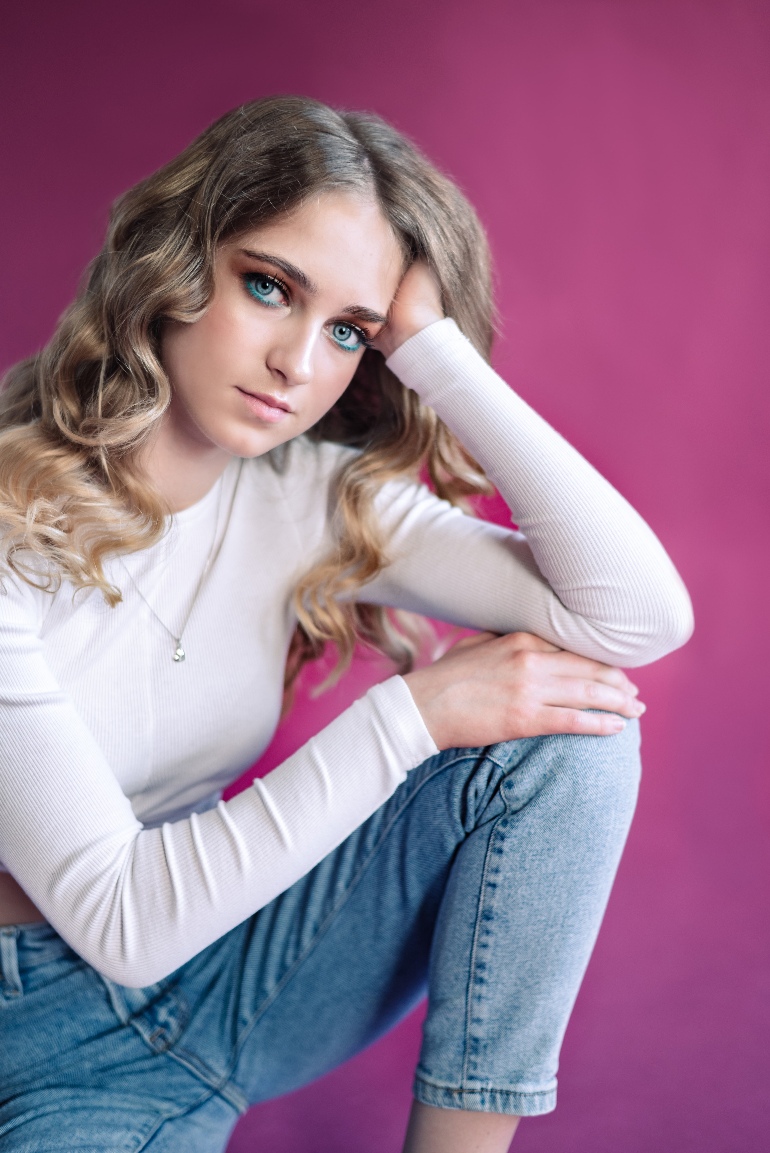 юная девушка в голубых джинсах и белой майке рука на колене на розовом фоне