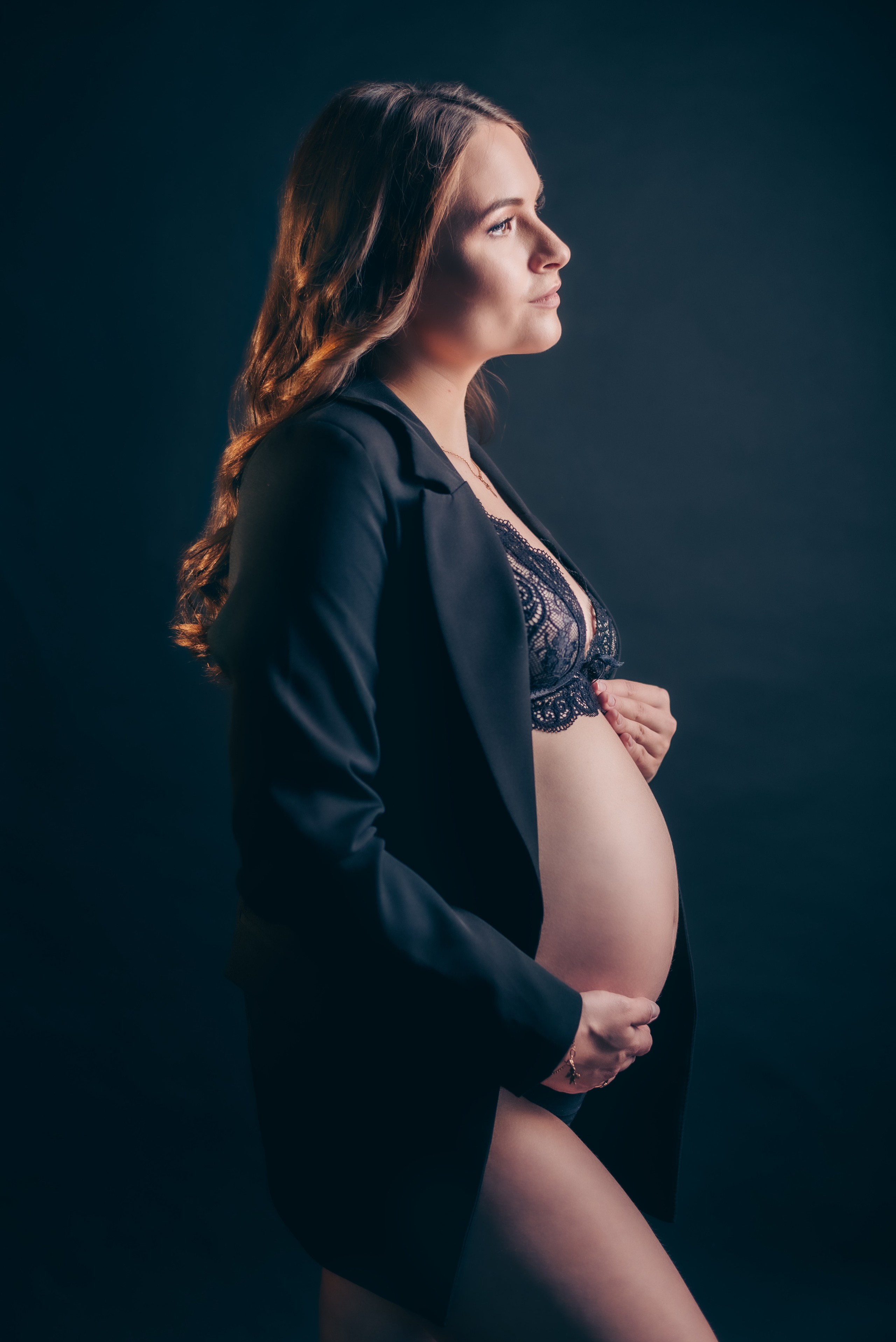 молодая беременная  женщина в жакете с оголенным животом сбоку