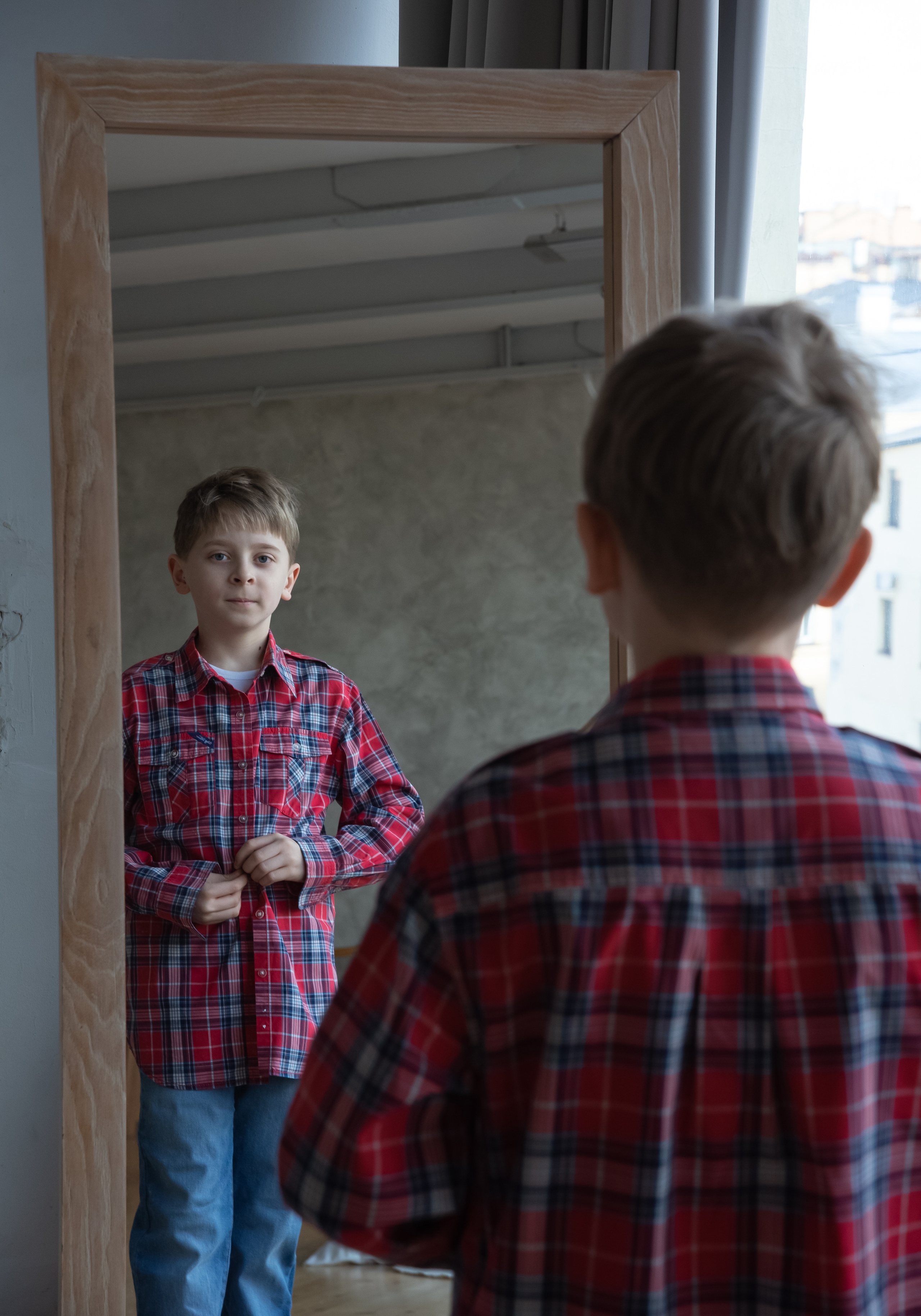 подросток у зеркала застегивает пуговицы на рубашке