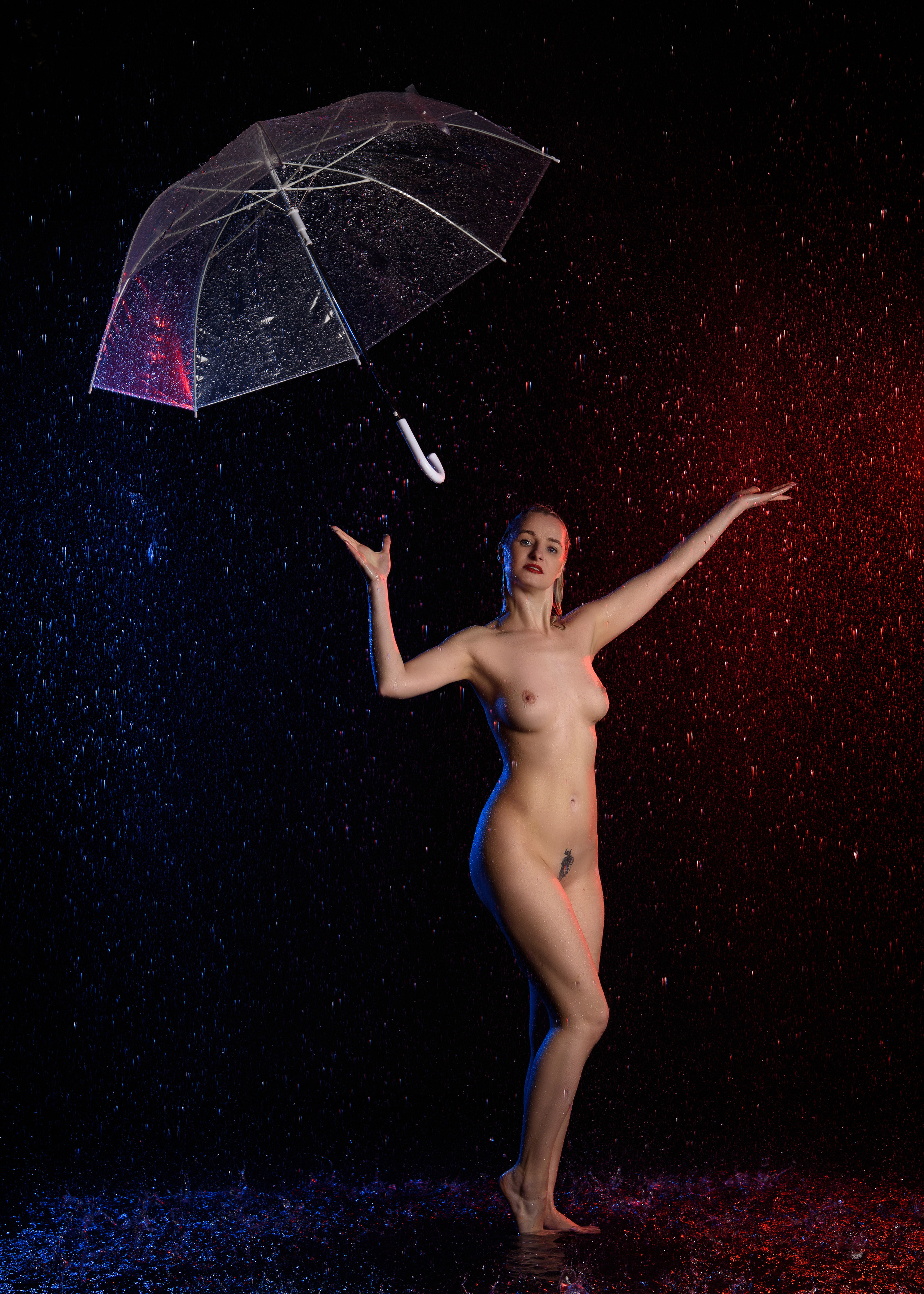 Обнаженная девушка под дождем с зонтом в фотостудии