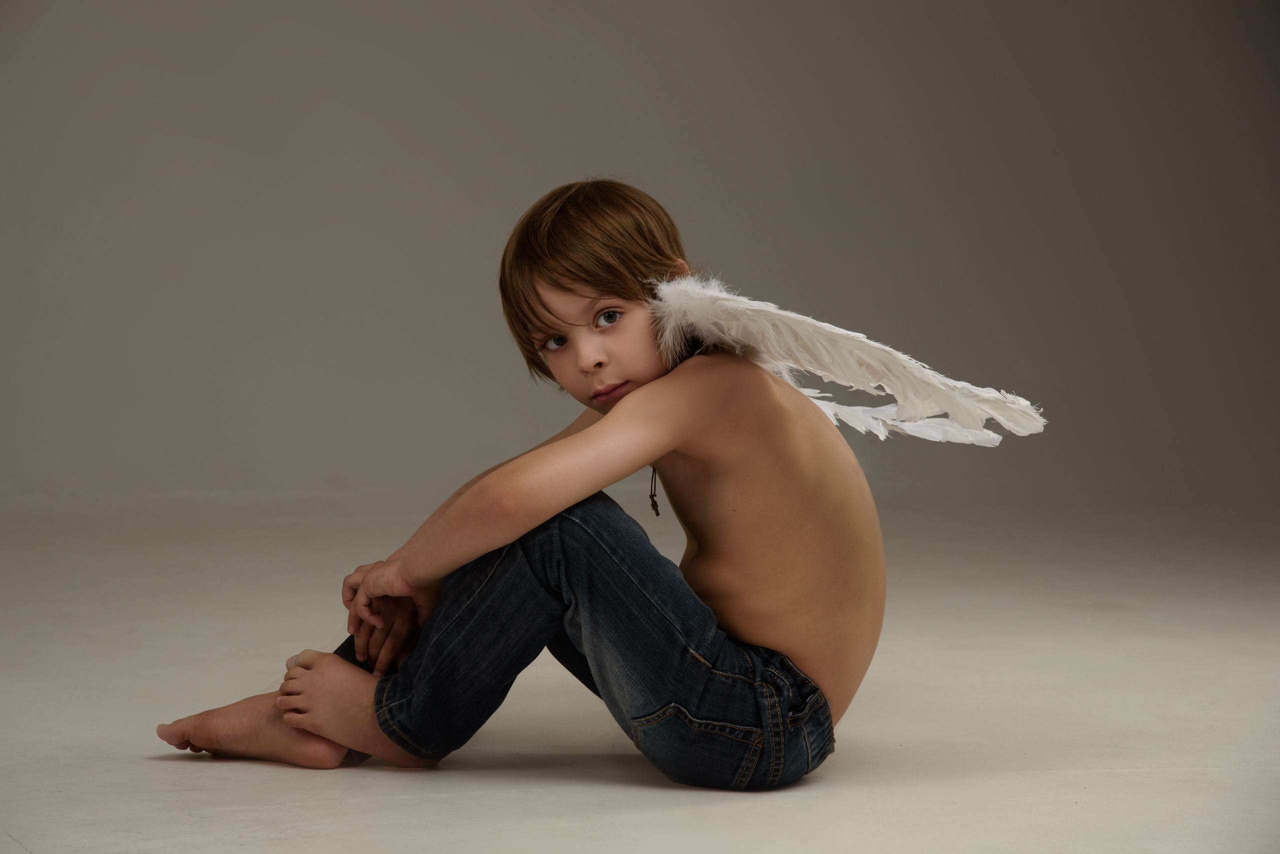 мальчик ангел сидит на полу обхватив руками колени