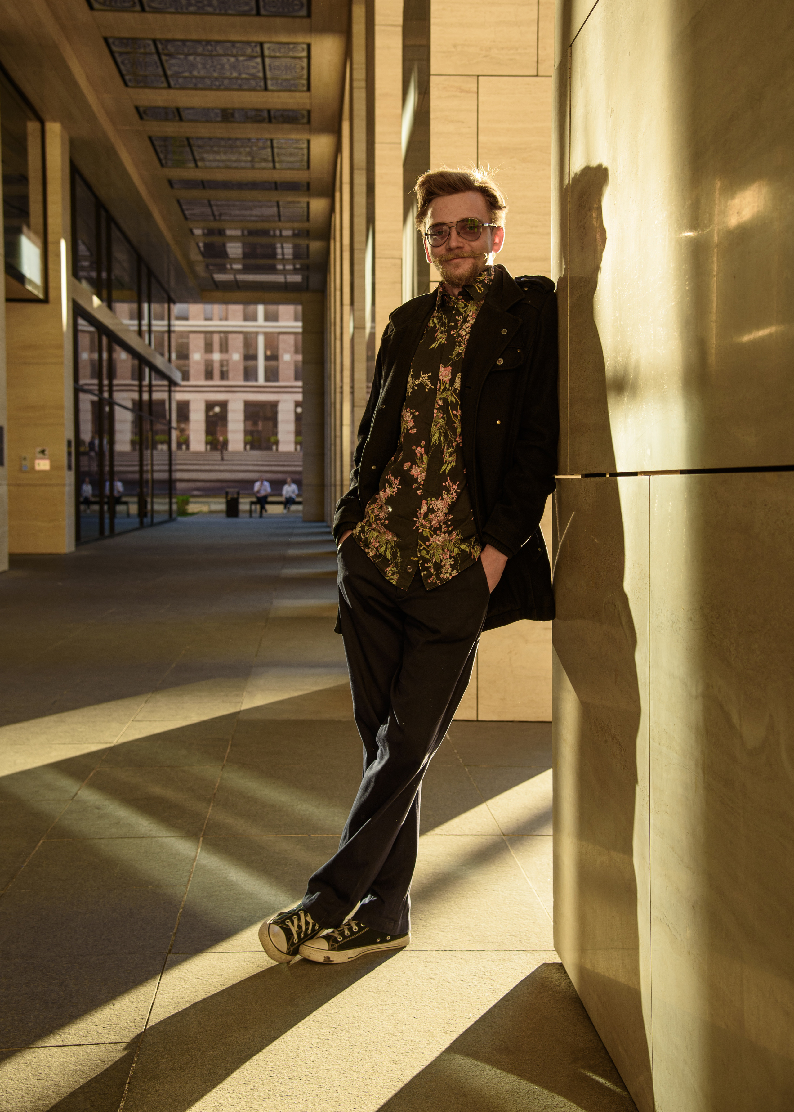 мужской портрет фотопрогулка в городе мужчина стоит облокотившись на колону в контровом свете стиль одежды casual