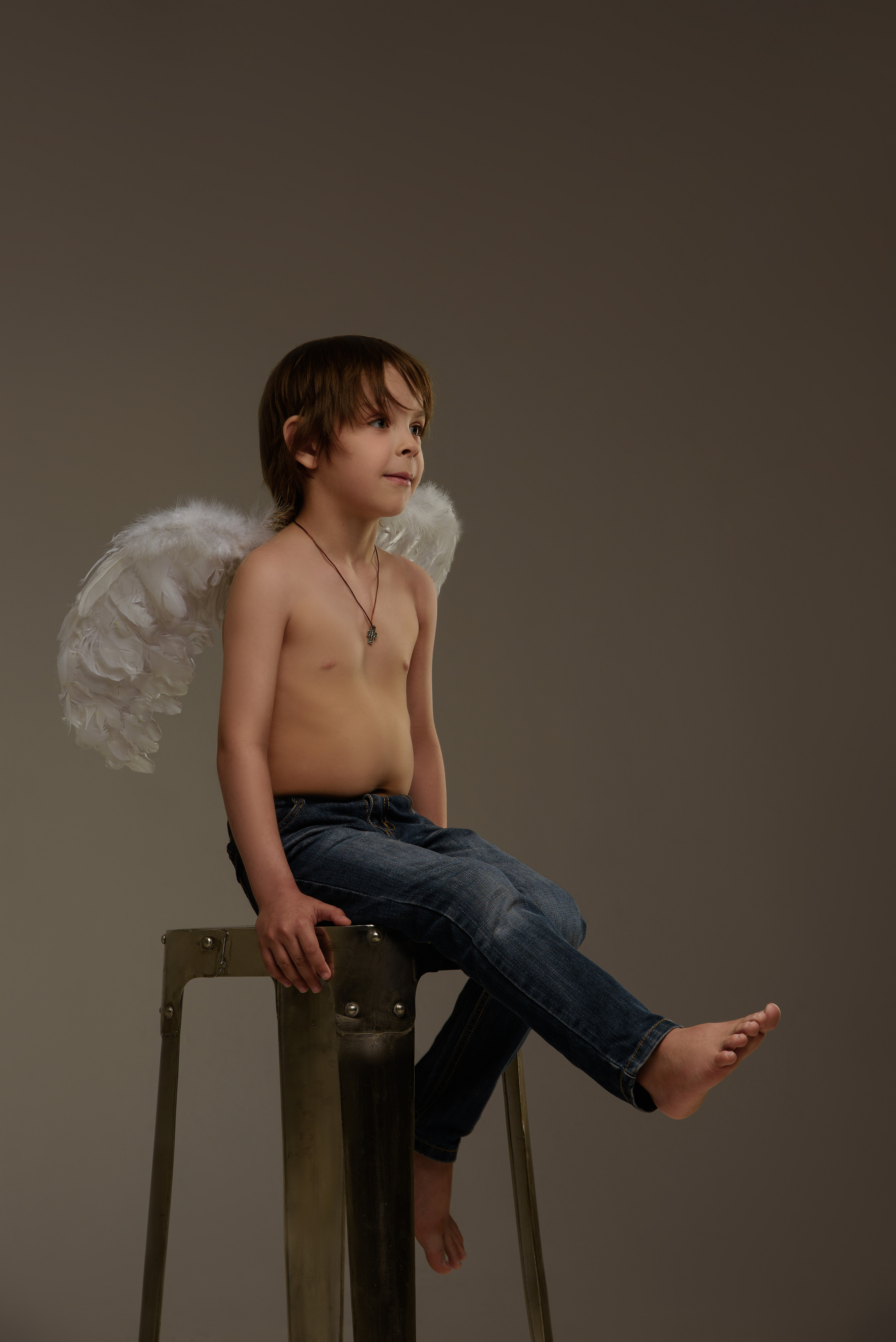 мальчик ангел сидит на высоком стуле и болтает ногами
