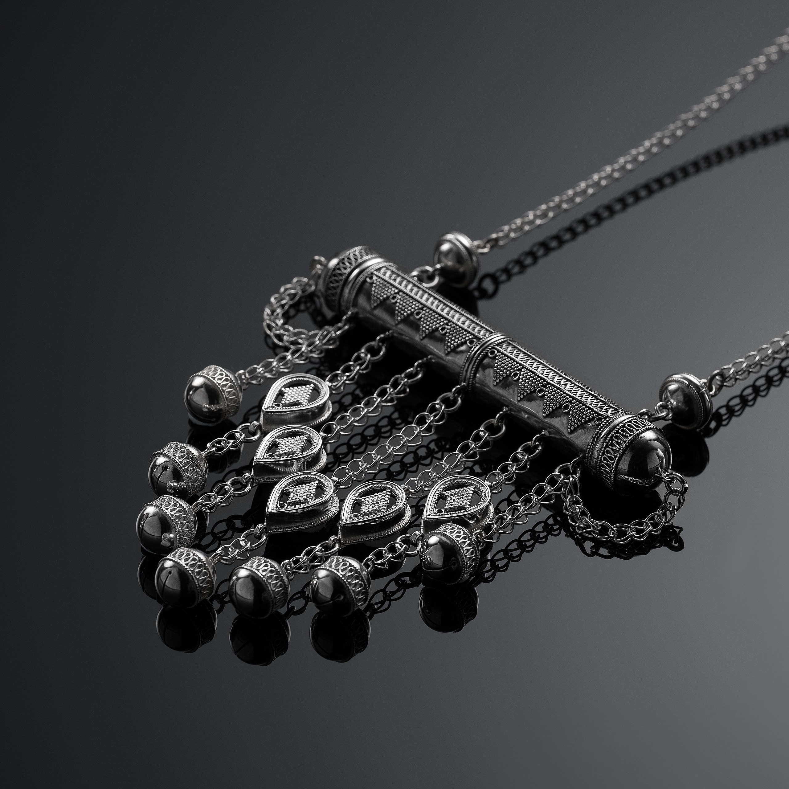 Рекламная фотосъёмка украшений Ornek — подвеска с цепями и символическими элементами. Минималистичный чёрный фон, акцент на текстуре и деталях изделия.