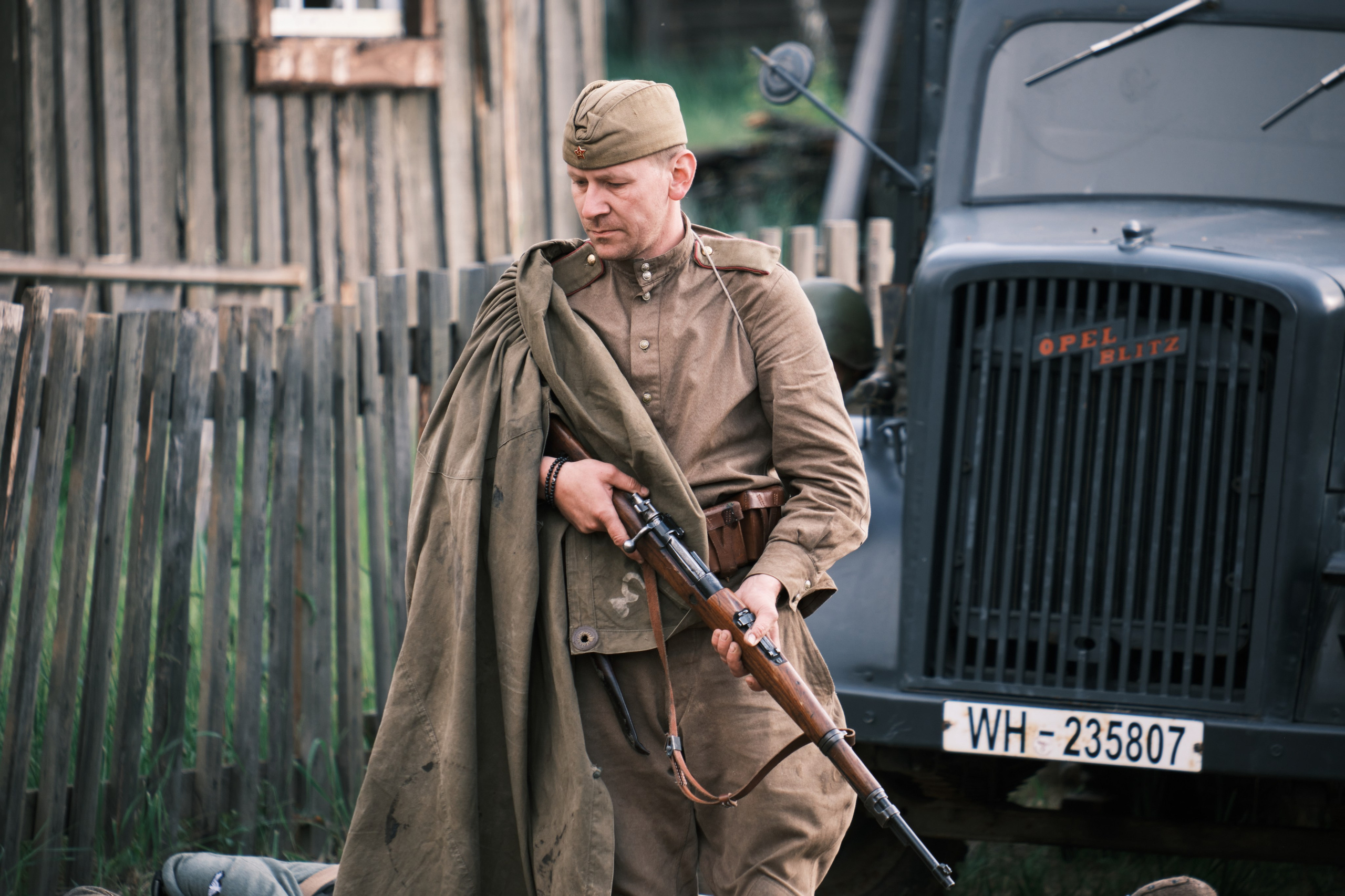 Русский солдат с ружьем идет на фоне немецкого автомобиля