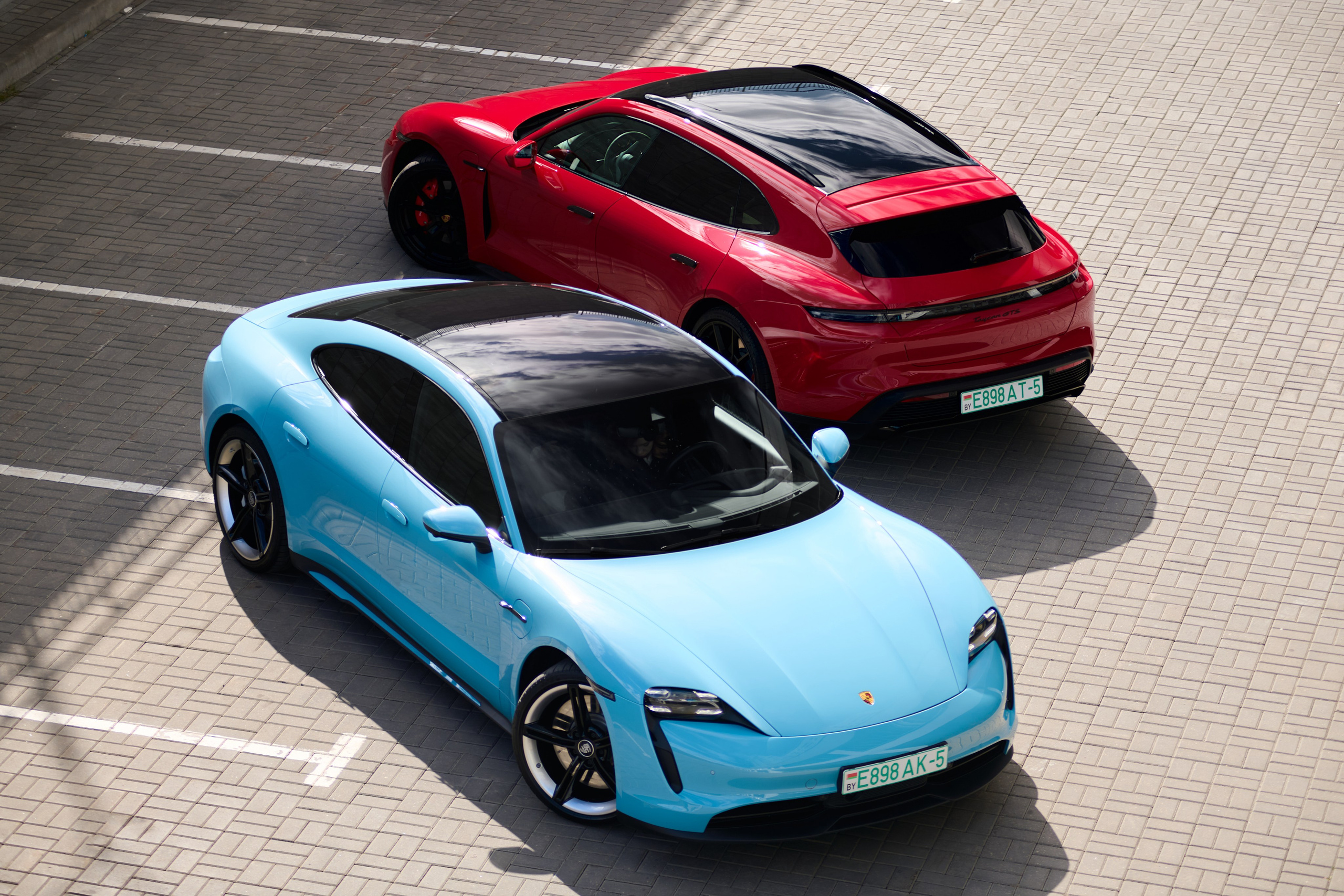 Голубой Porsche Taycan 4S и красный Porsche Taycan GTS на парковке, вид сверху