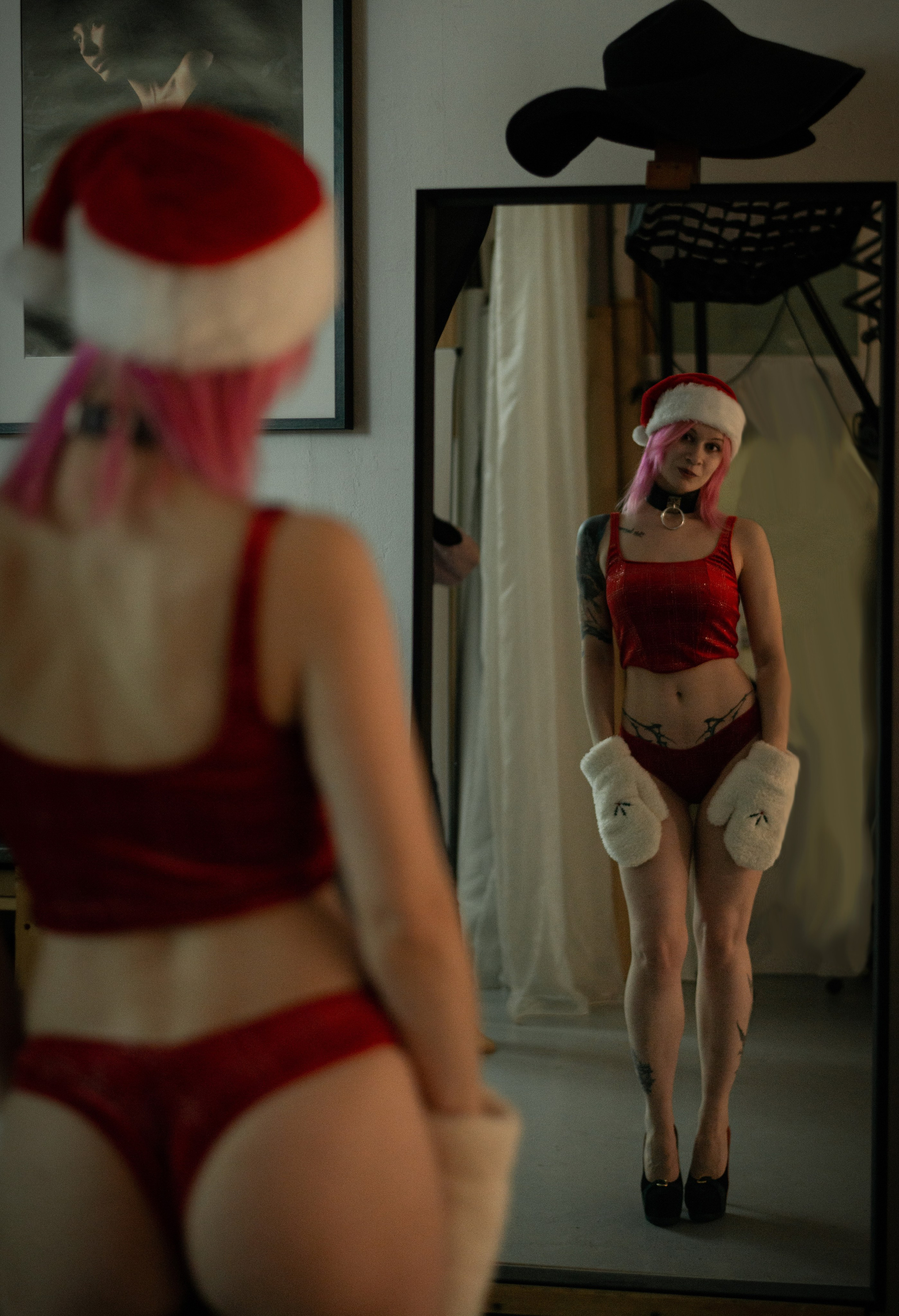 девушка в новогоднем красном белье шапке деда мороза и варежках стоит смотрит на свое отражение в большом зеркале
