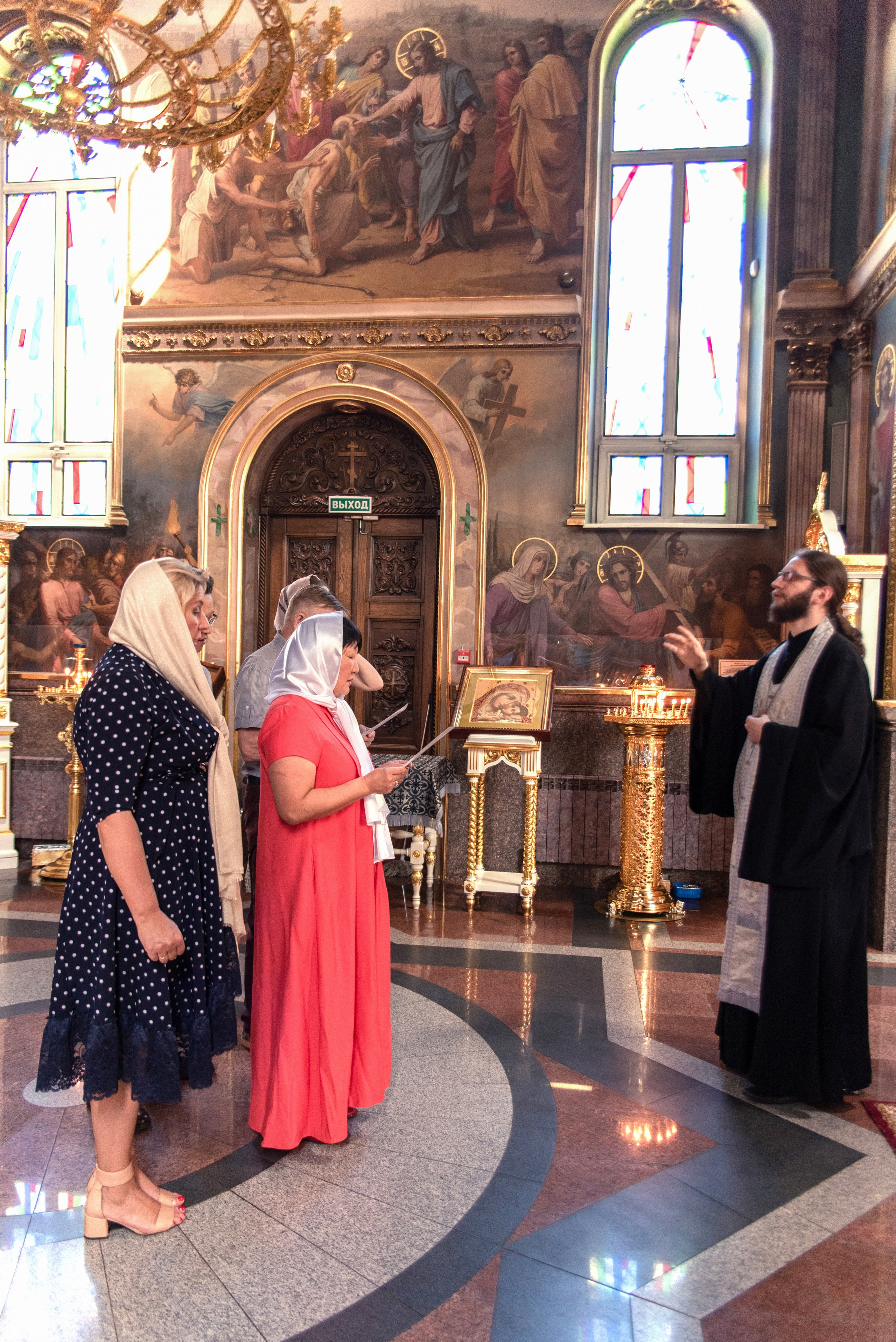 Священник читает молитву на крещении в храме. Фото на фоне витражных окон 