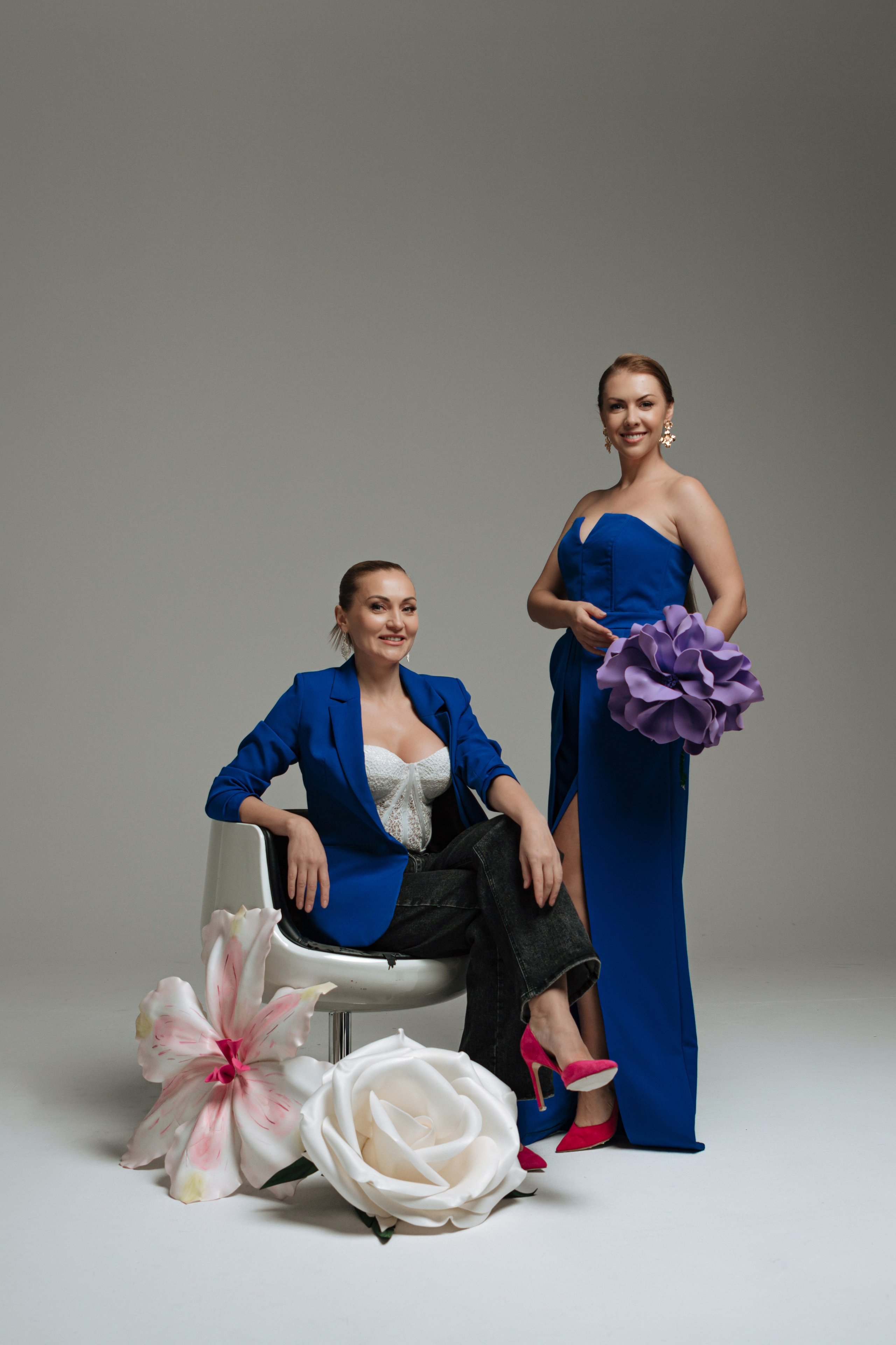  В студии царит атмосфера творчества и весеннего настроения. Две модели позируют перед объективом в элегантных синих нарядах. Их платья и пиджаки контрастируют с мягким освещением и белыми циклорамами, создавая ощущение свежести и обновления. Фотограф ловит самые выразительные ракурсы, запечатлевая образы, пронизанные духом пробуждающейся природы.