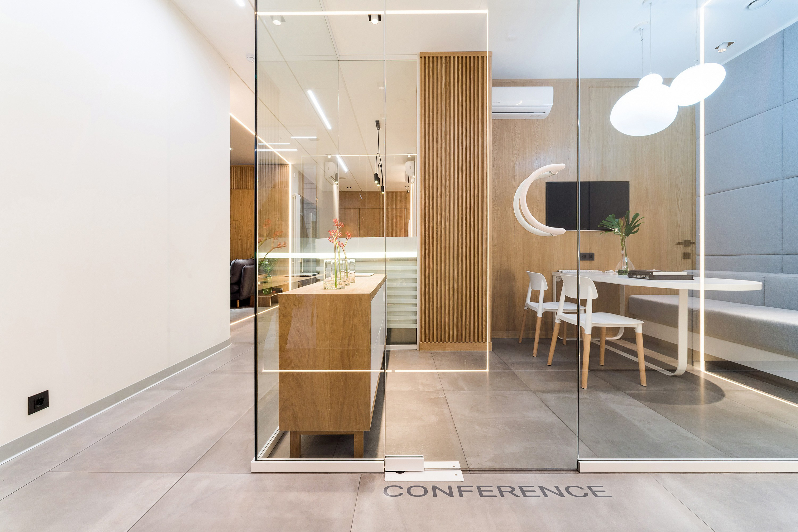 дизайн интерьера стоматологической клиники выполнен в современном минималистичном стиле с теплой домашней атмосферой. Текстуры дерева, наливной пол, яркие акценты, чистота линий, модульная сетка, стеклянные перегородки