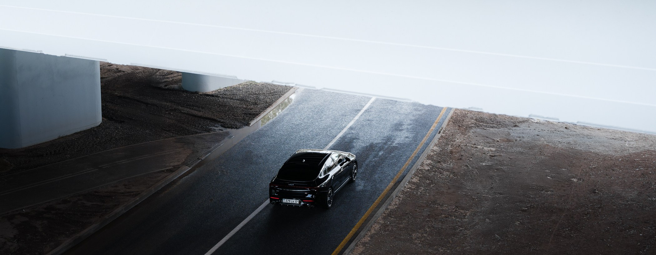 Urban-фотография из Астаны: машина движется по пустой трассе под эстакадой после дождя.