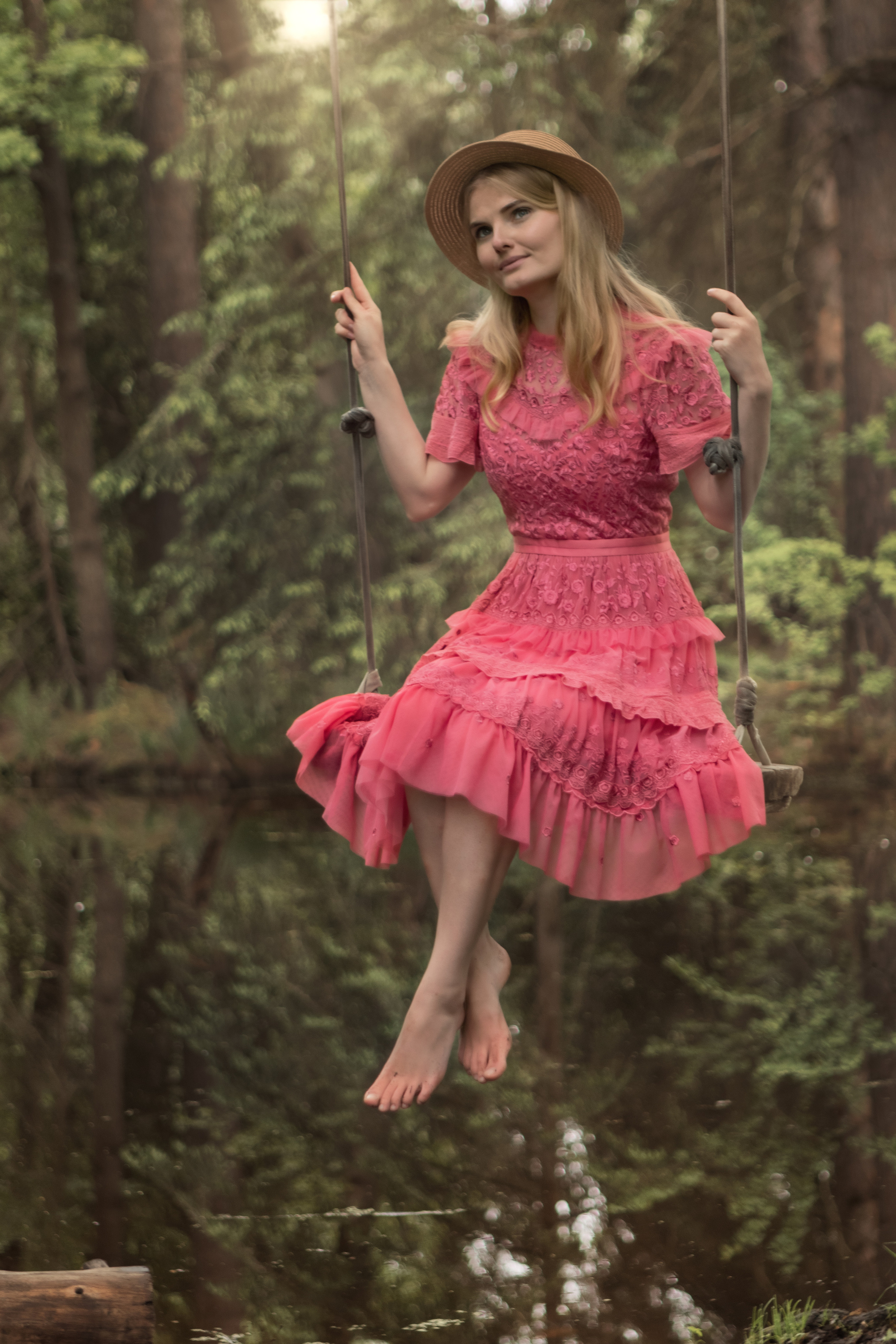 Девушка в полный рост в розовом платье на качелях в лесу