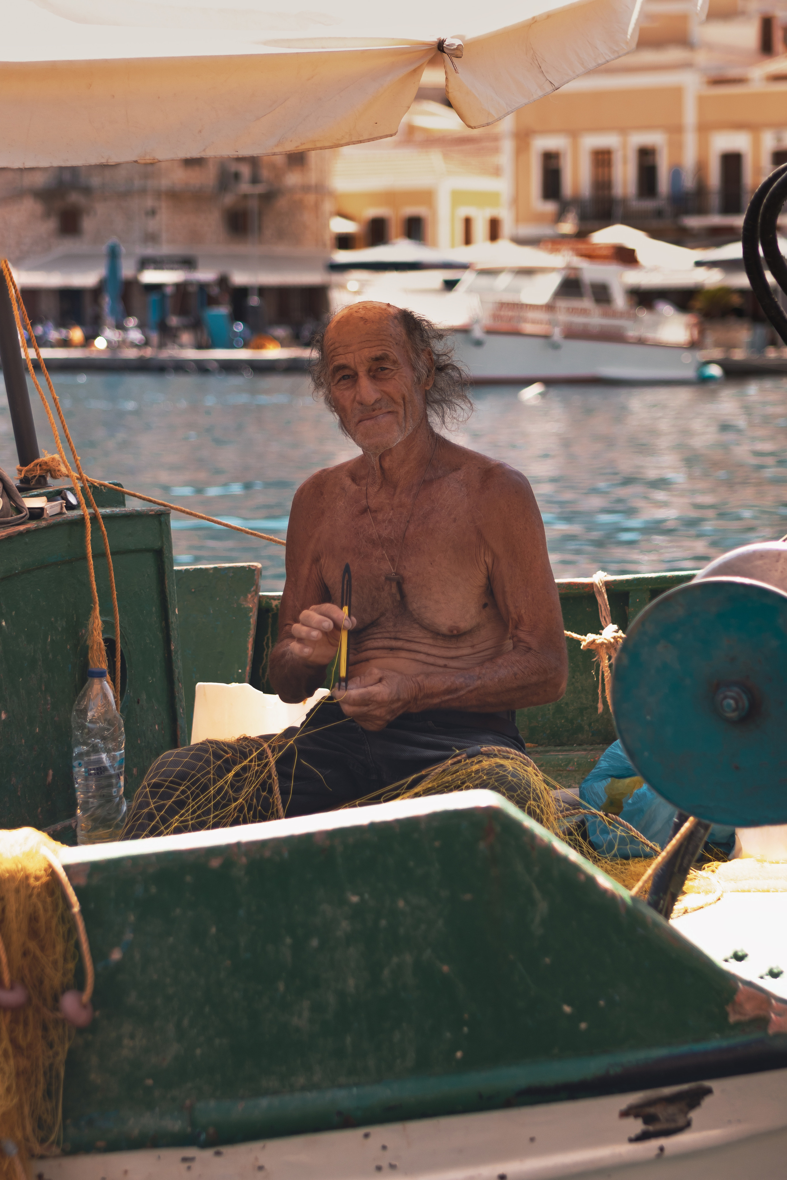 Старый рыбак в лодке плетет сети