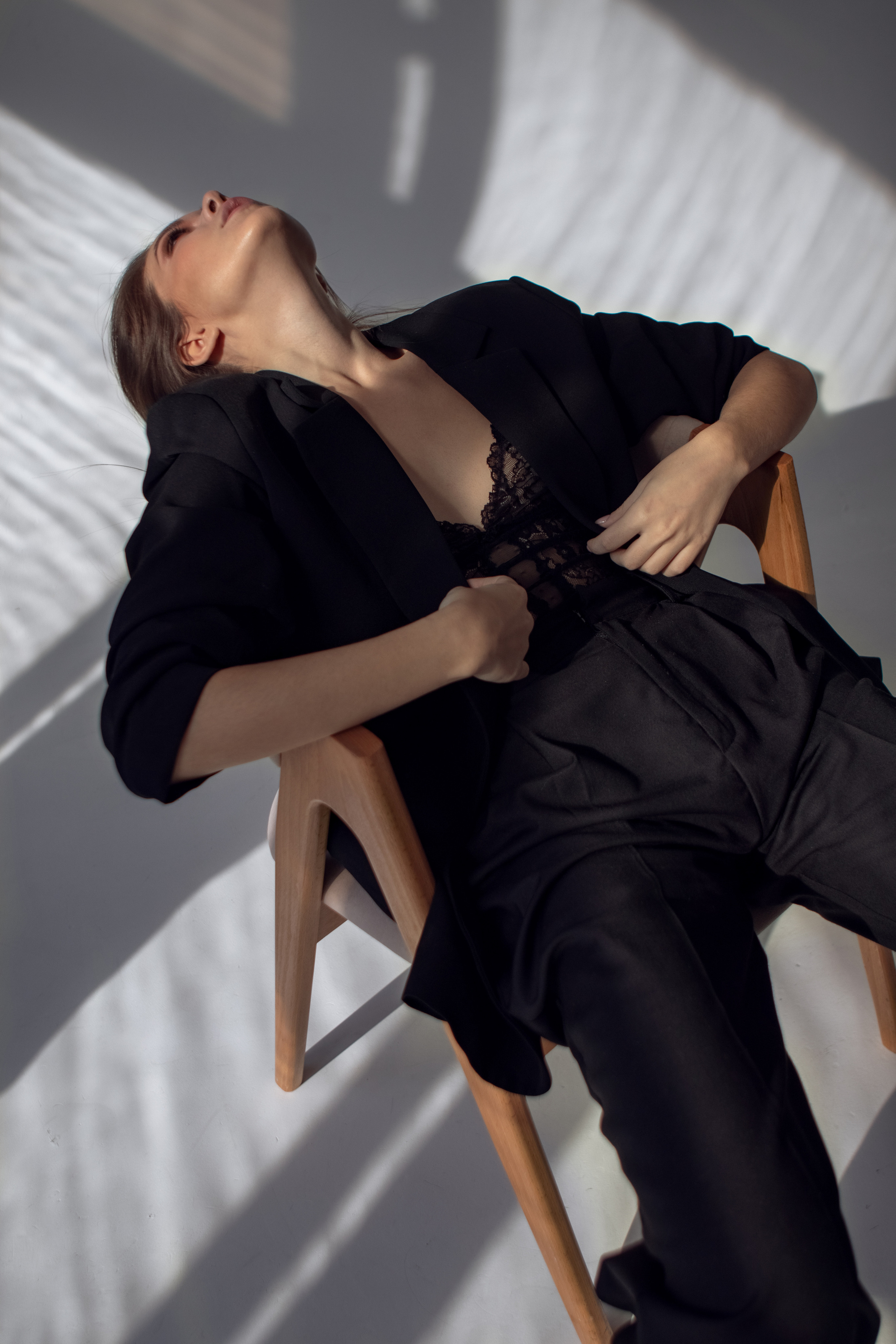 Девушка в черном сидит на стуле на белой циклораме 