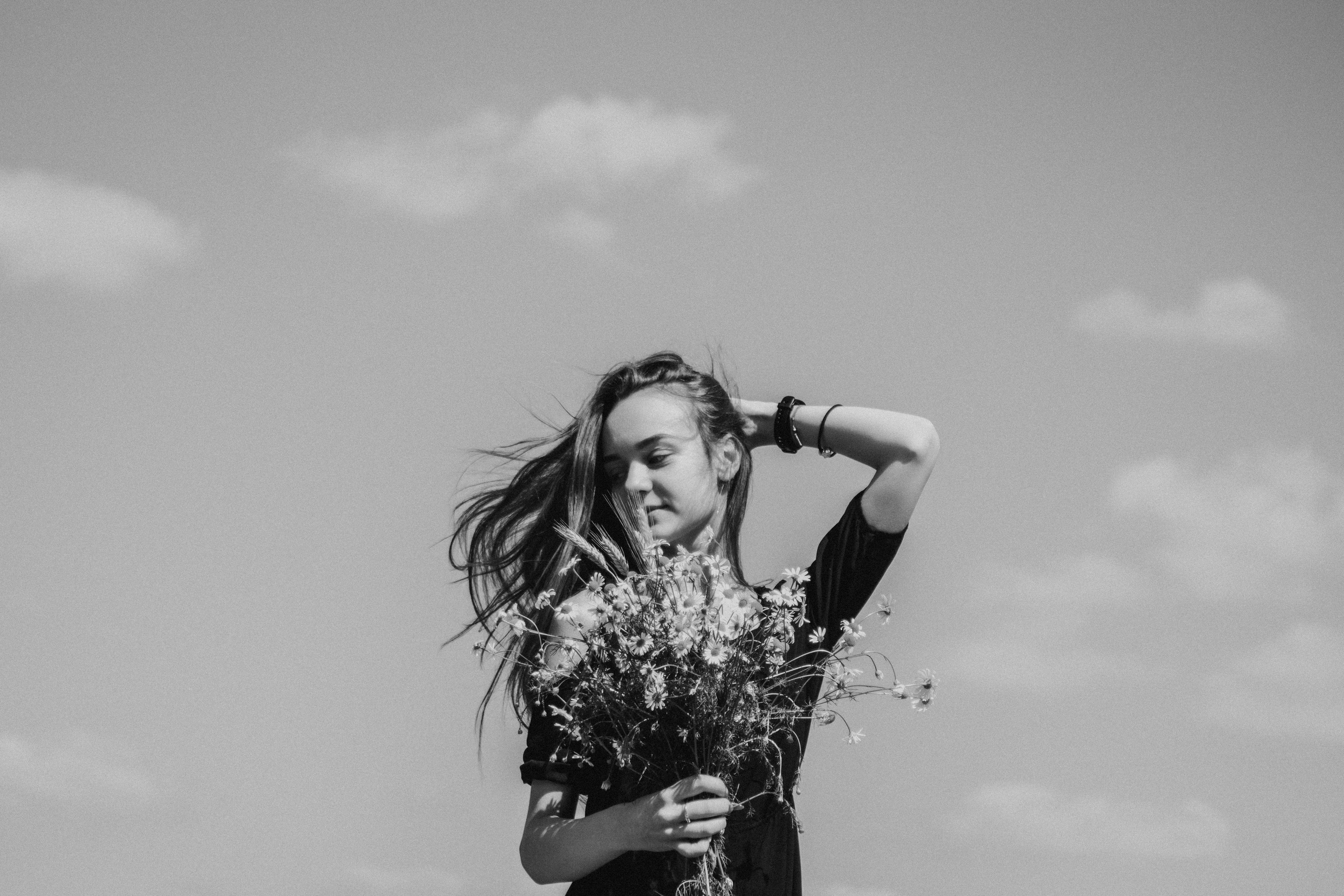 Черно белый портрет девушки на фоне неба с букетом ромашек