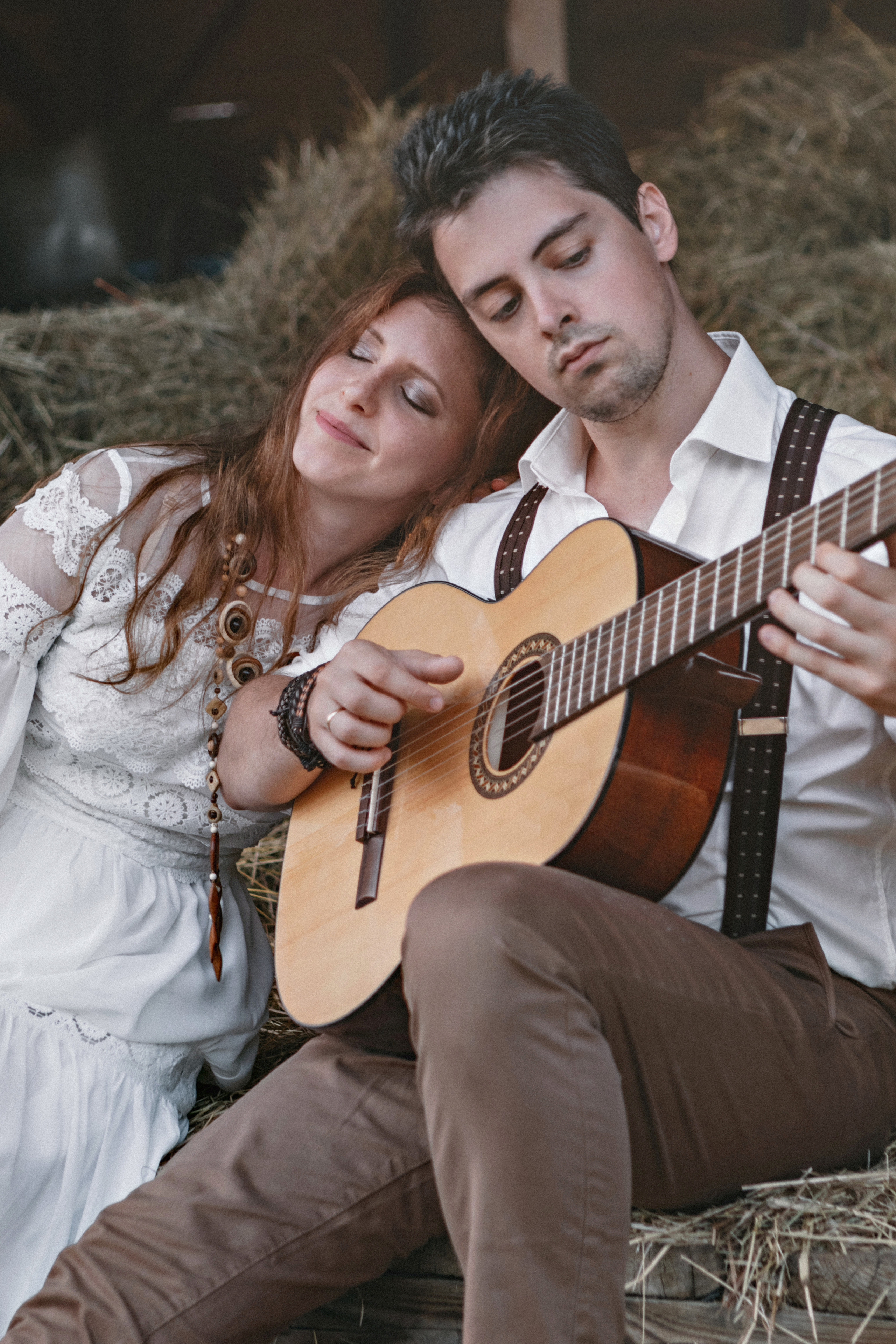 Влюбленная пара в белом играет на гитаре на сеновале