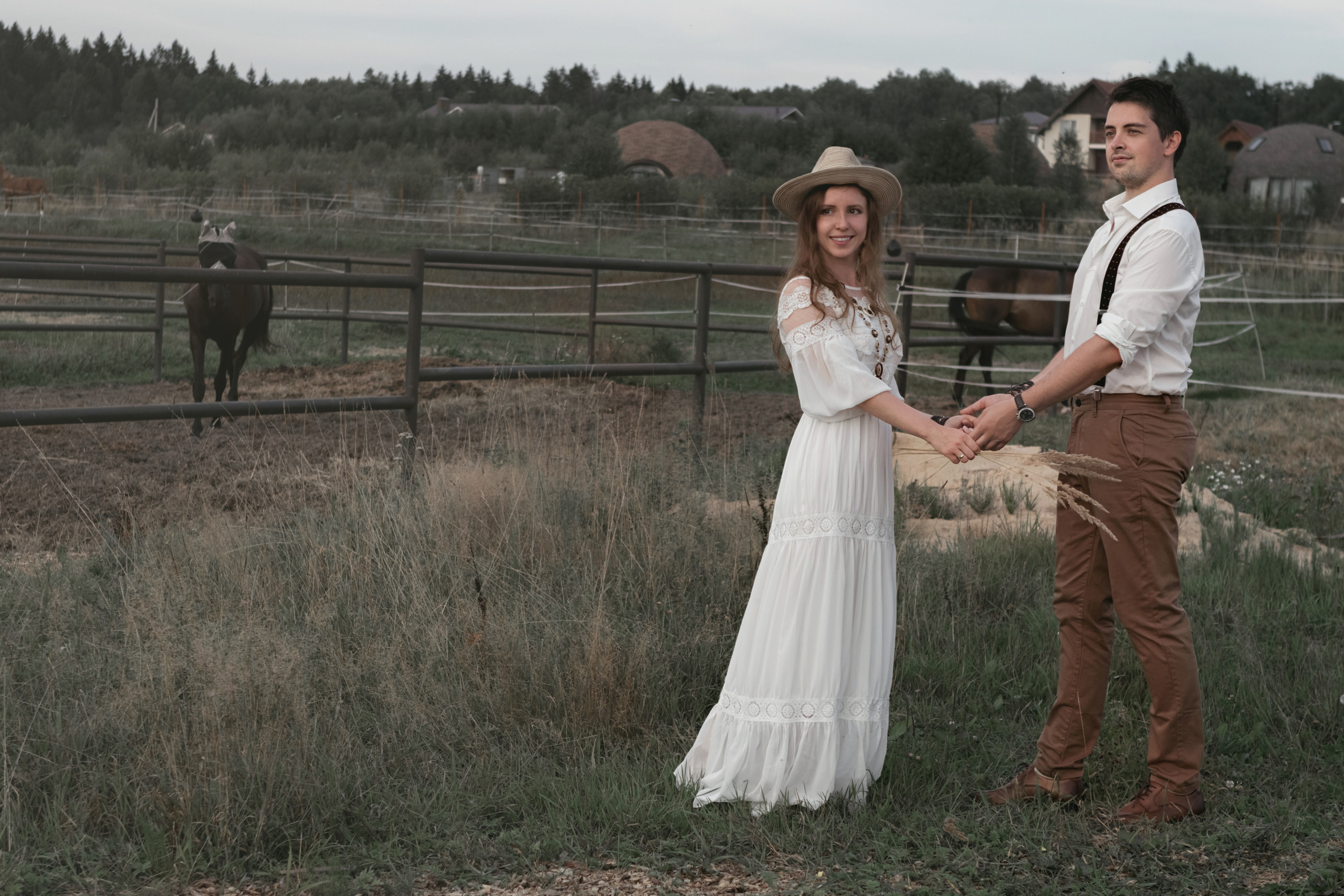 Влюбленная пара в белом держаться за руки на фоне лошади