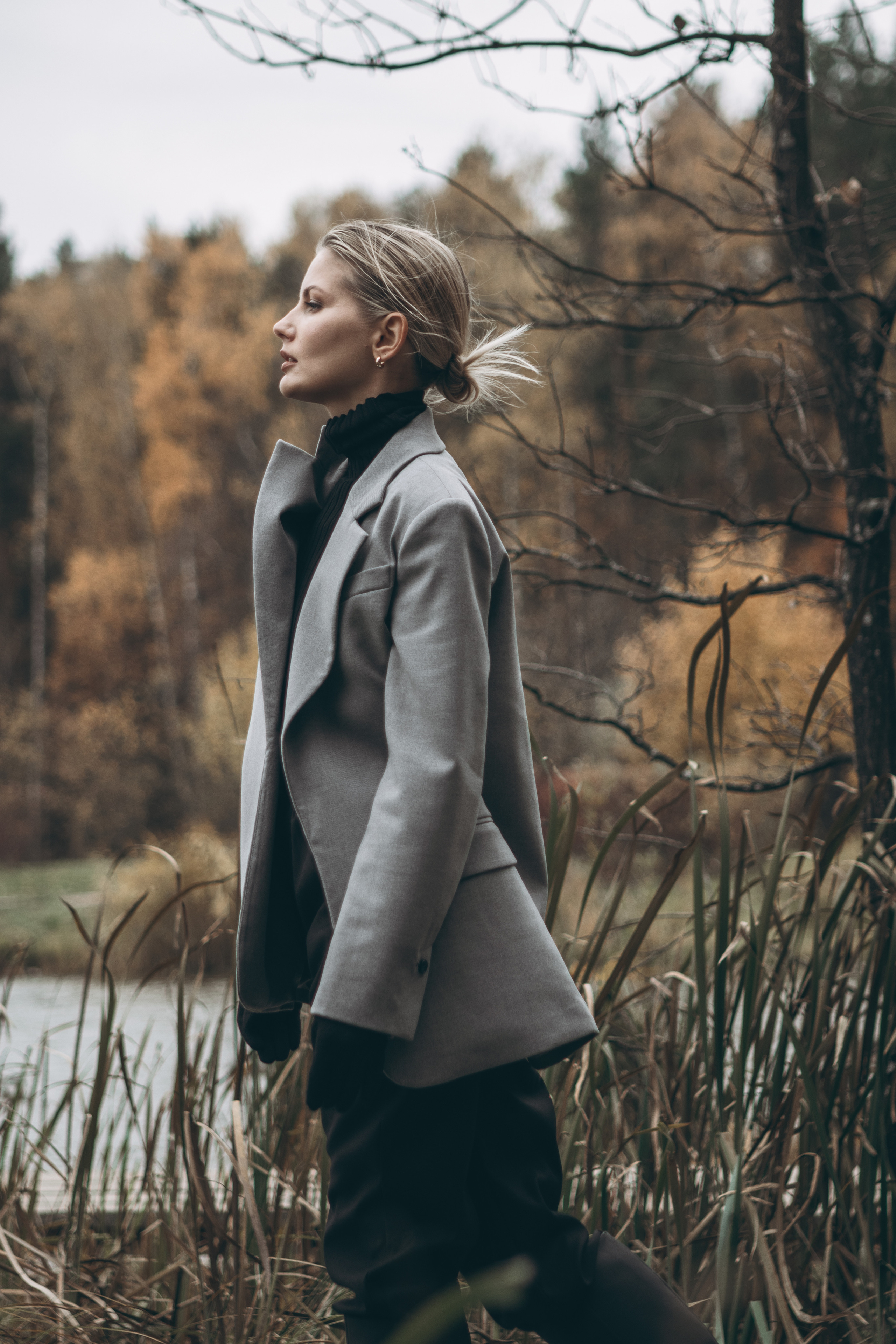 Девушка в пиджаке идет по мосту на фоне парка и пруда