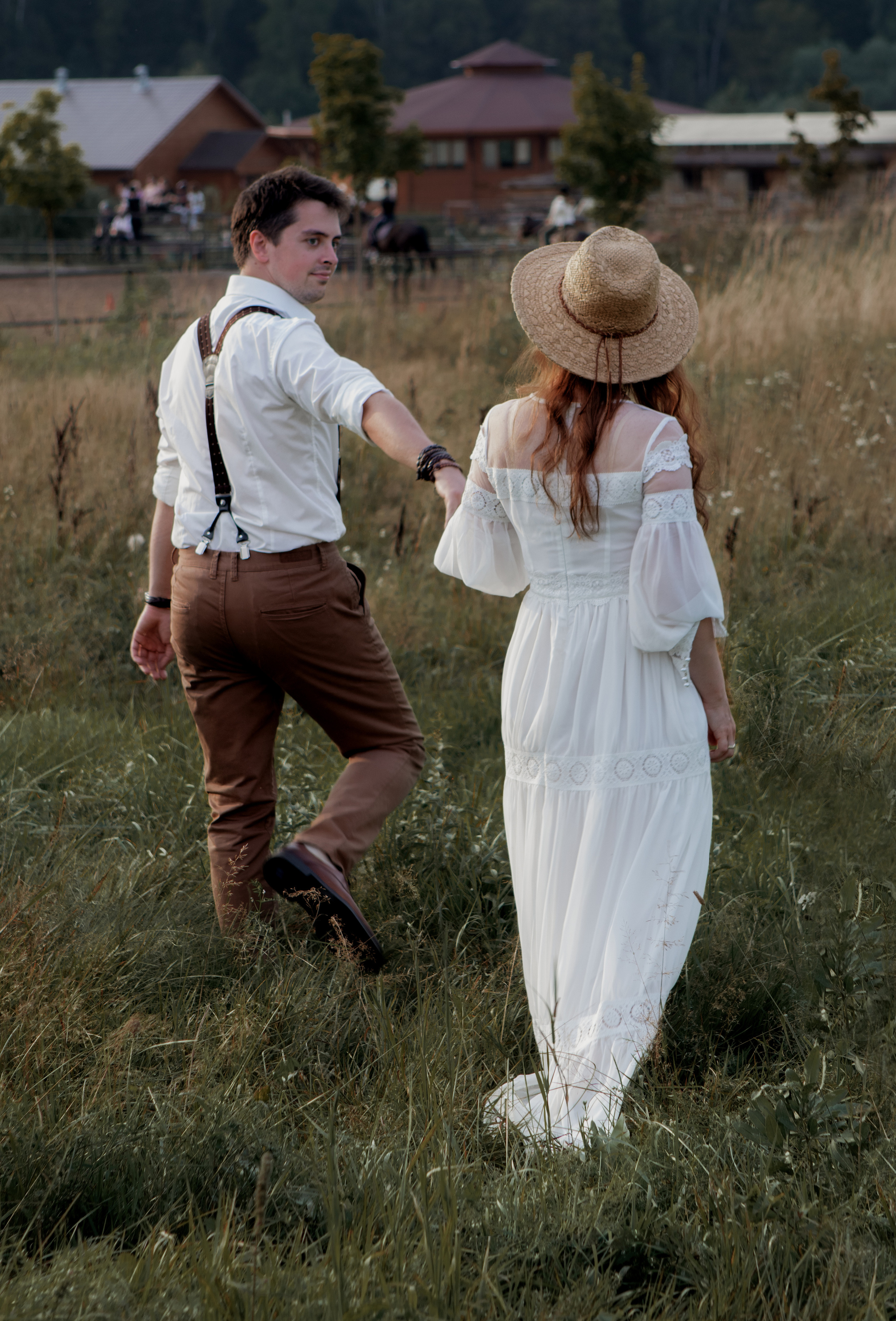 Влюбленная пара в белом идут за руку по полю