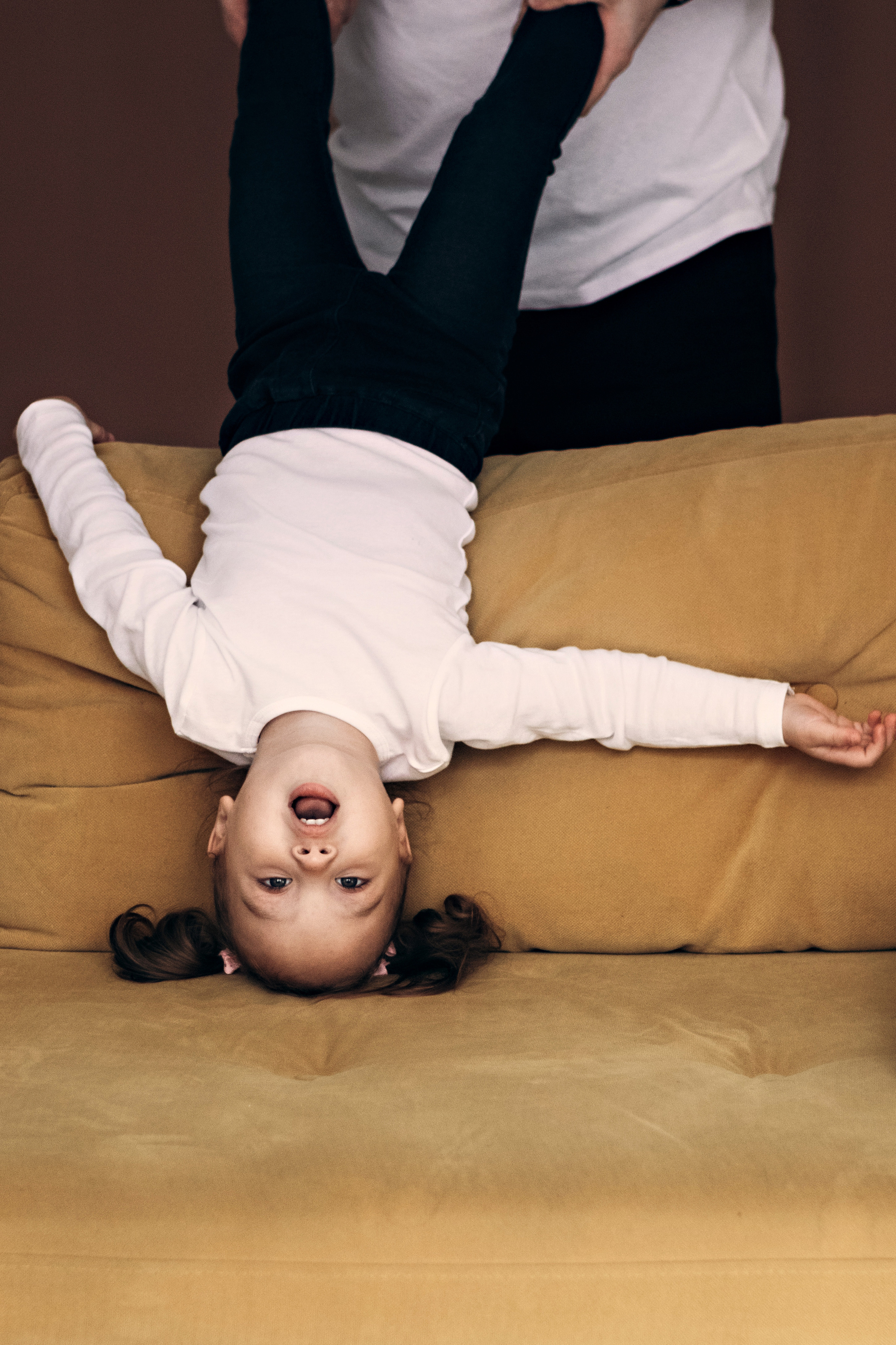 Маленькая девочка в белом вверх ногами на желтом диване