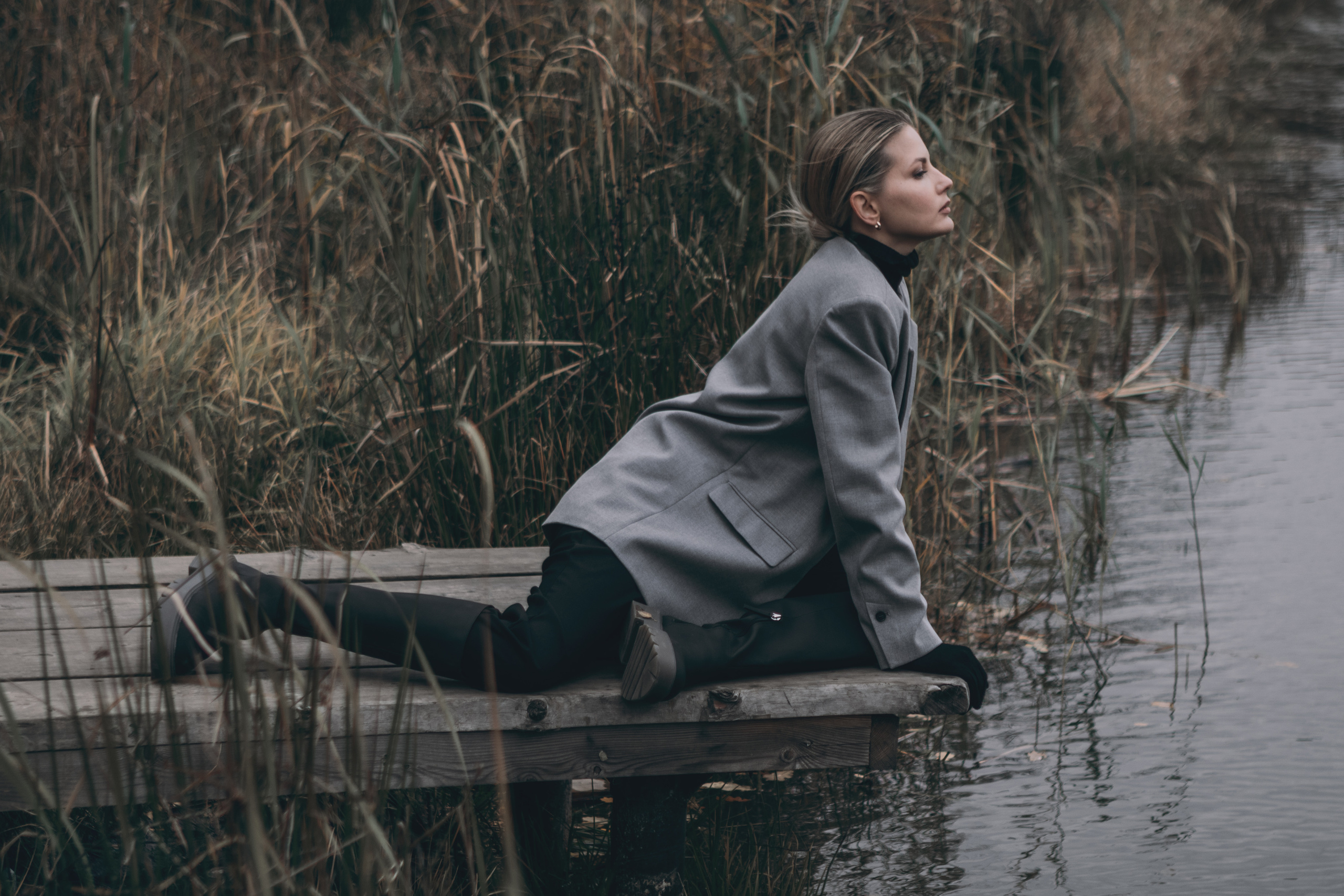 Девушка в пиджаке сидит на мосту над речкой
