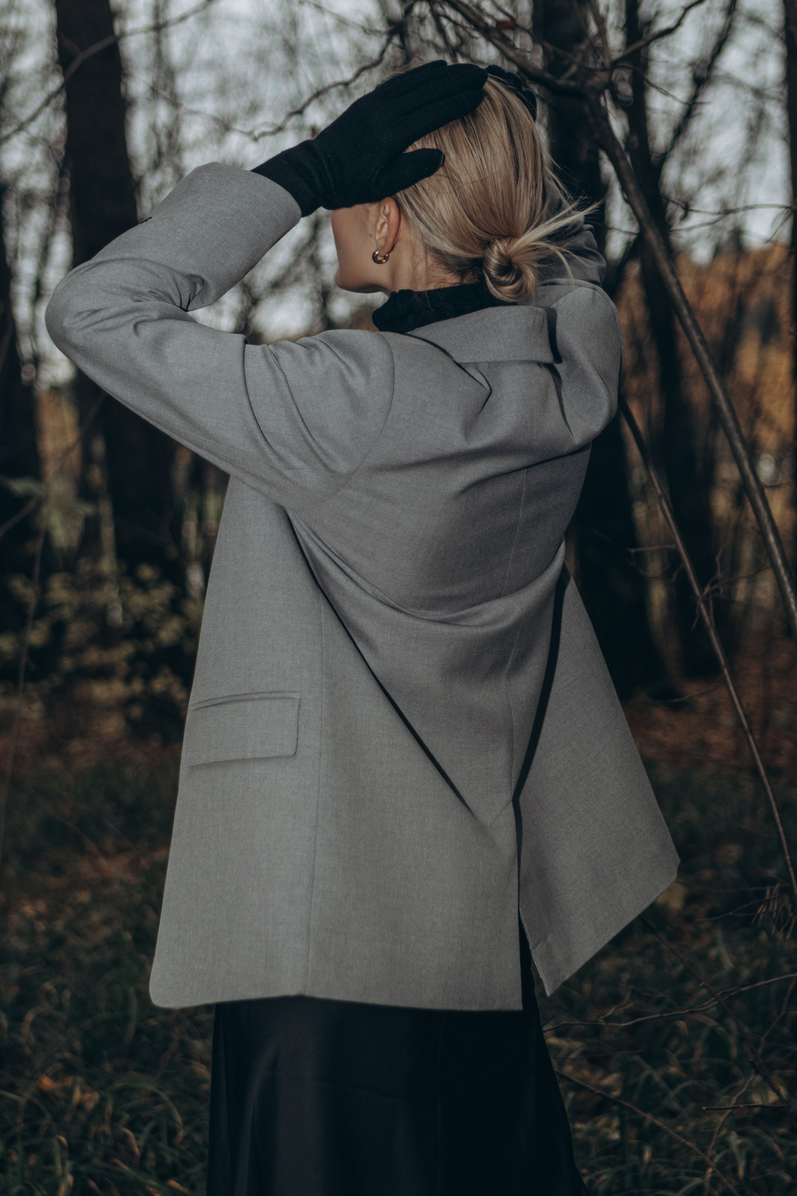 Девушка в пиджаке стоит спиной в осеннем лесу