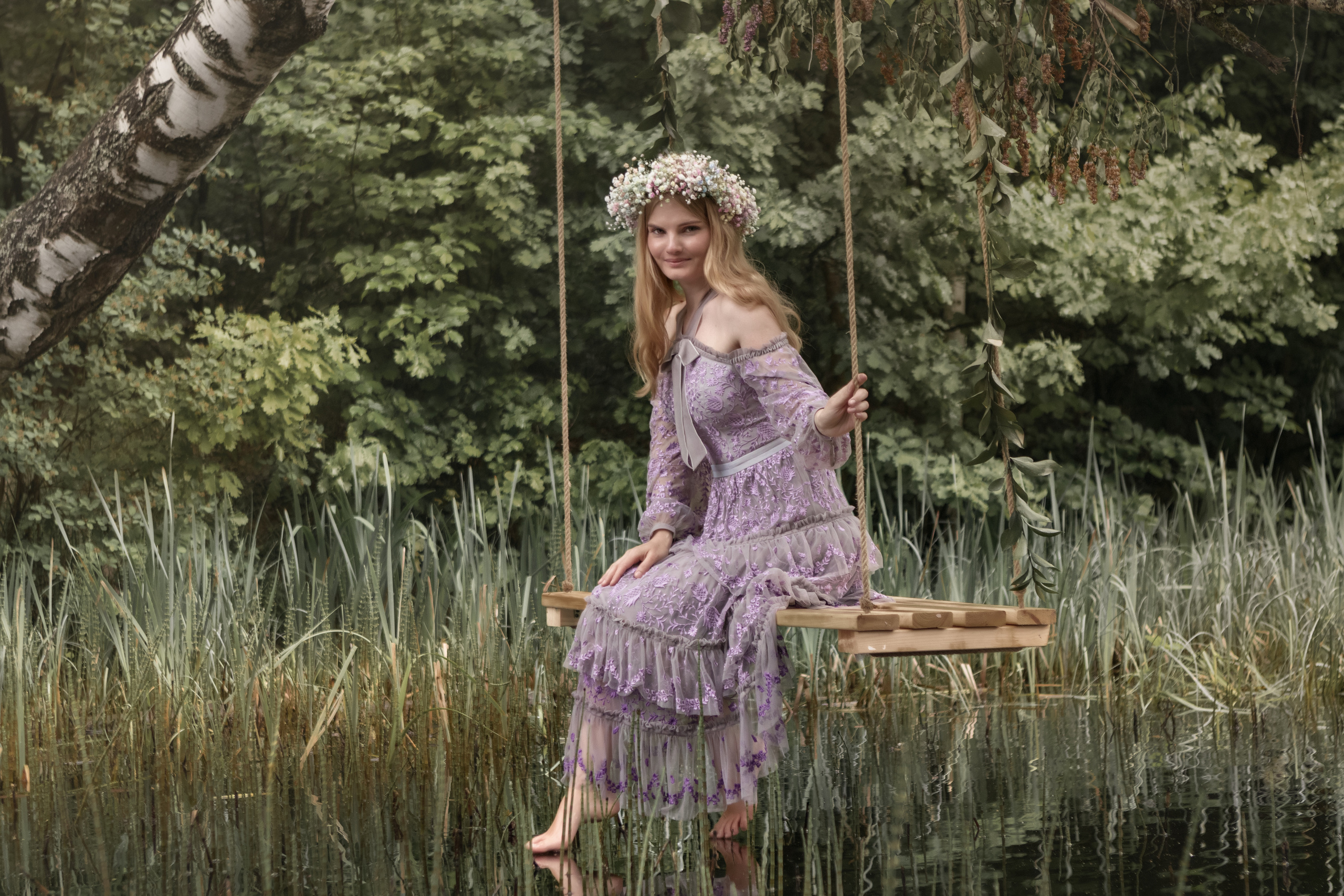 Девушка на качелях над рекой в лесу