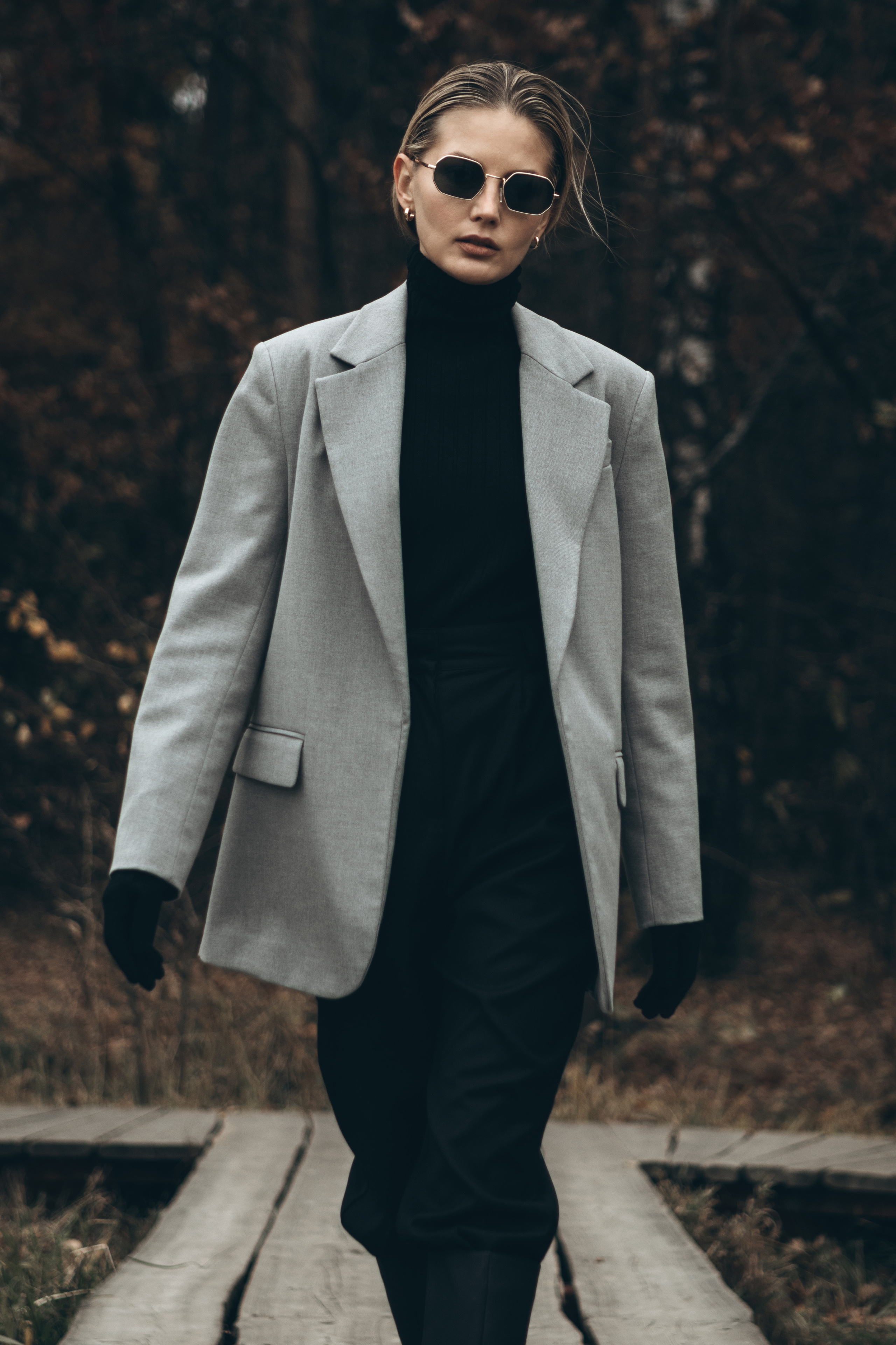 Девушка в пиджаке идет по мосту на фоне парка