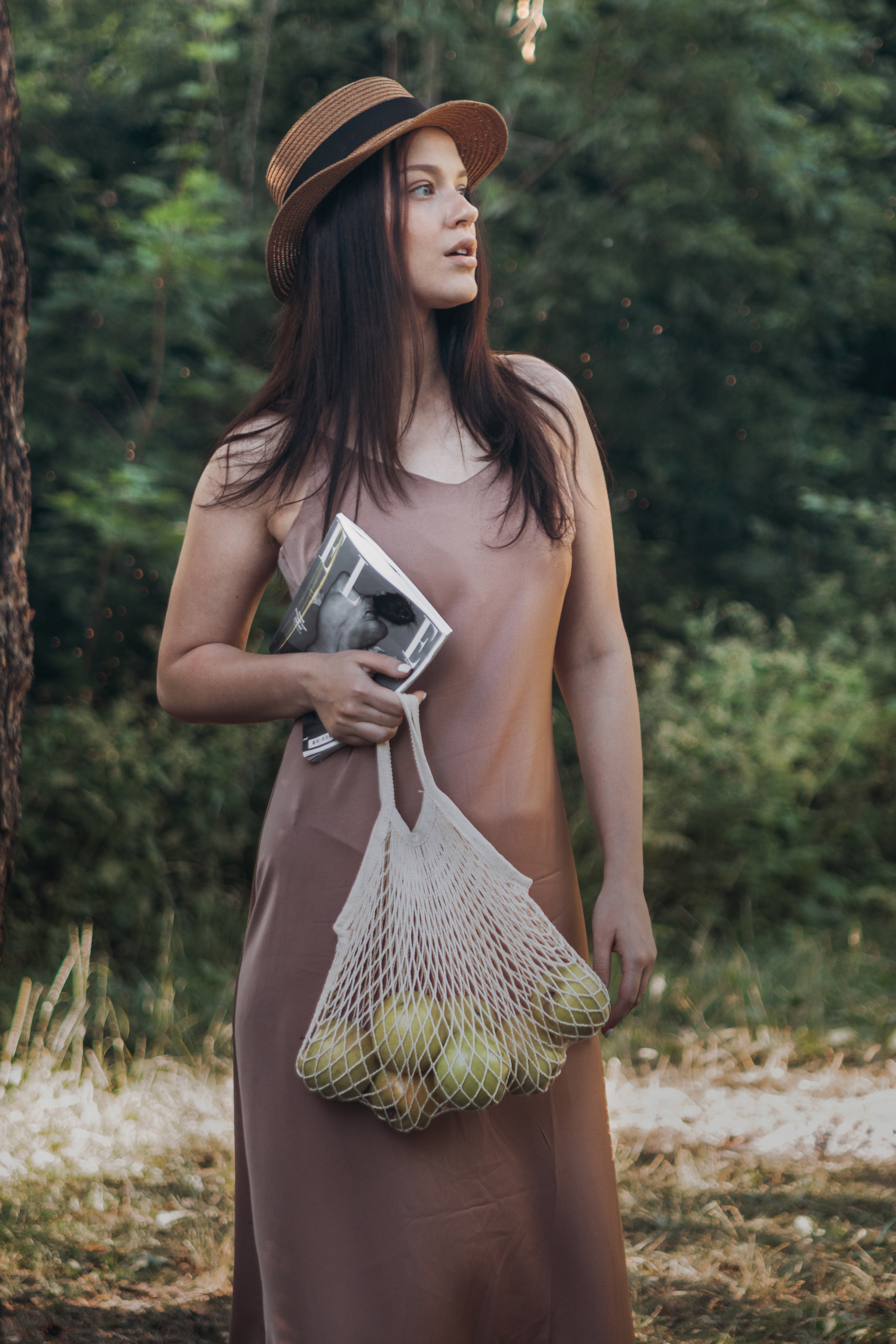 Девушка на природе с авоськой яблок и журналом в руках