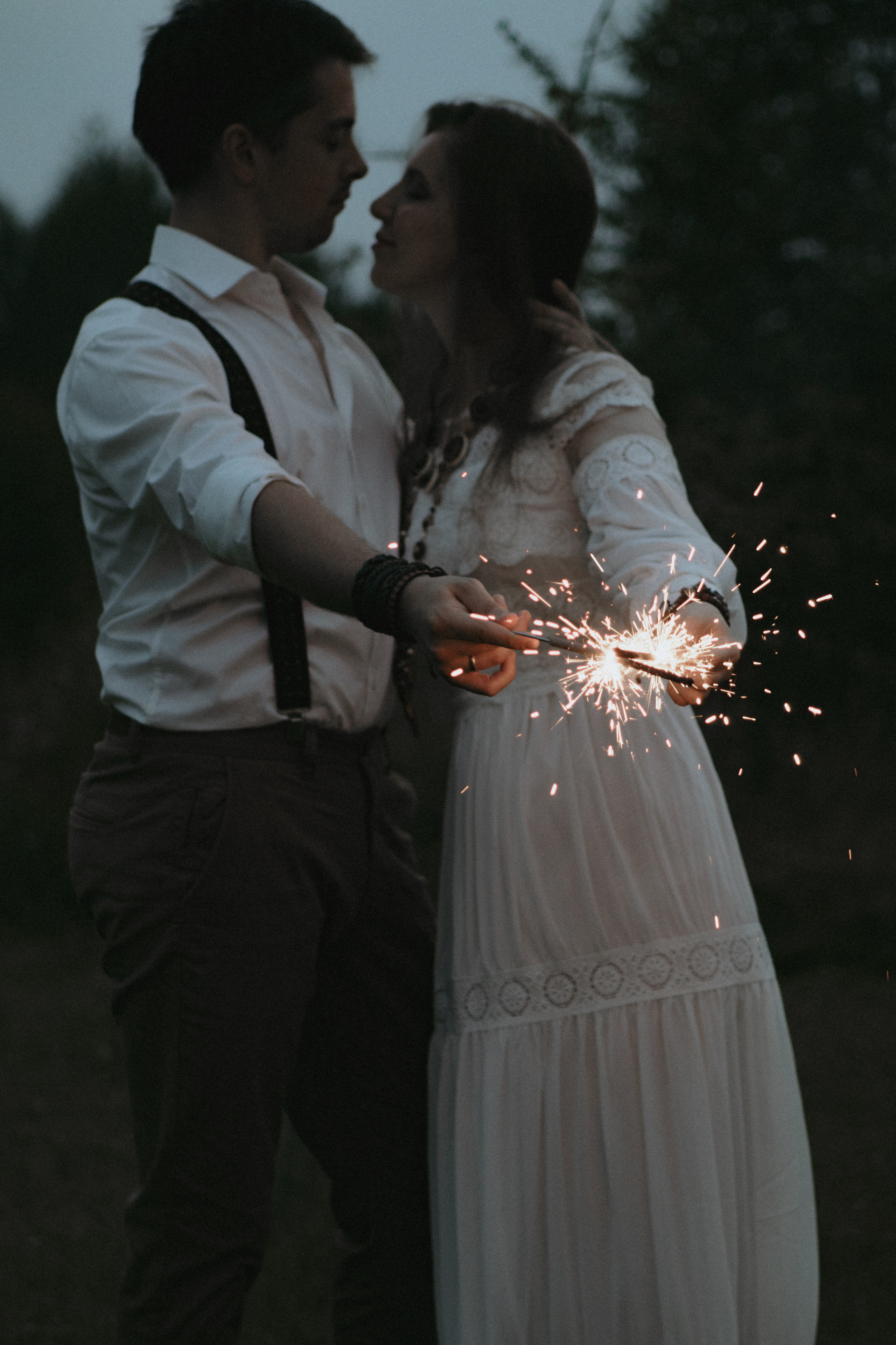 Влюбленная пара в белом держат в руках бенгальский огни