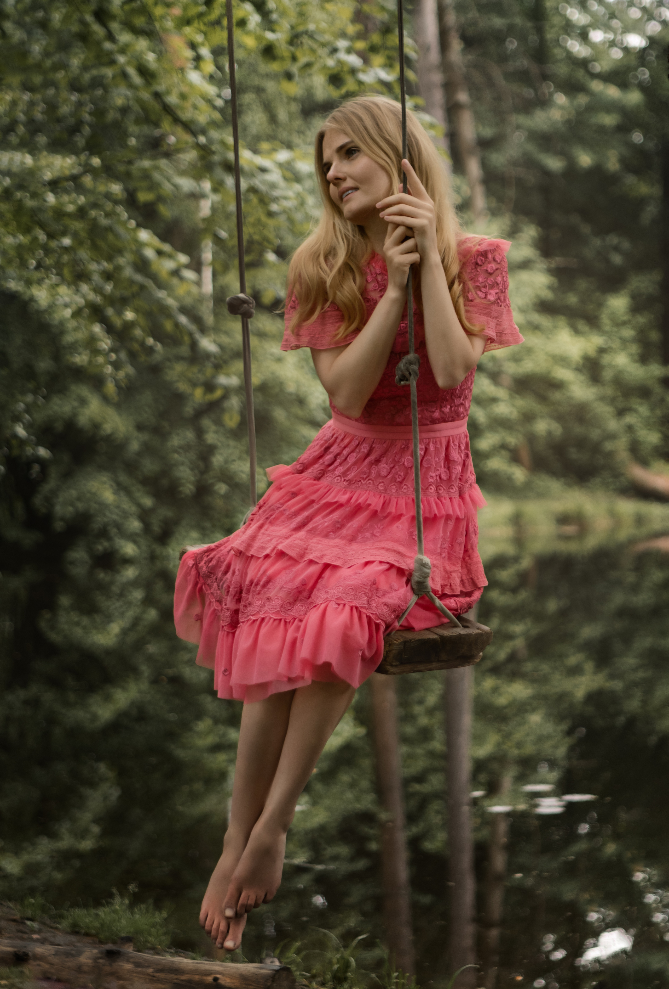 Девушка в полный рост в розовом платье на качелях в лесу