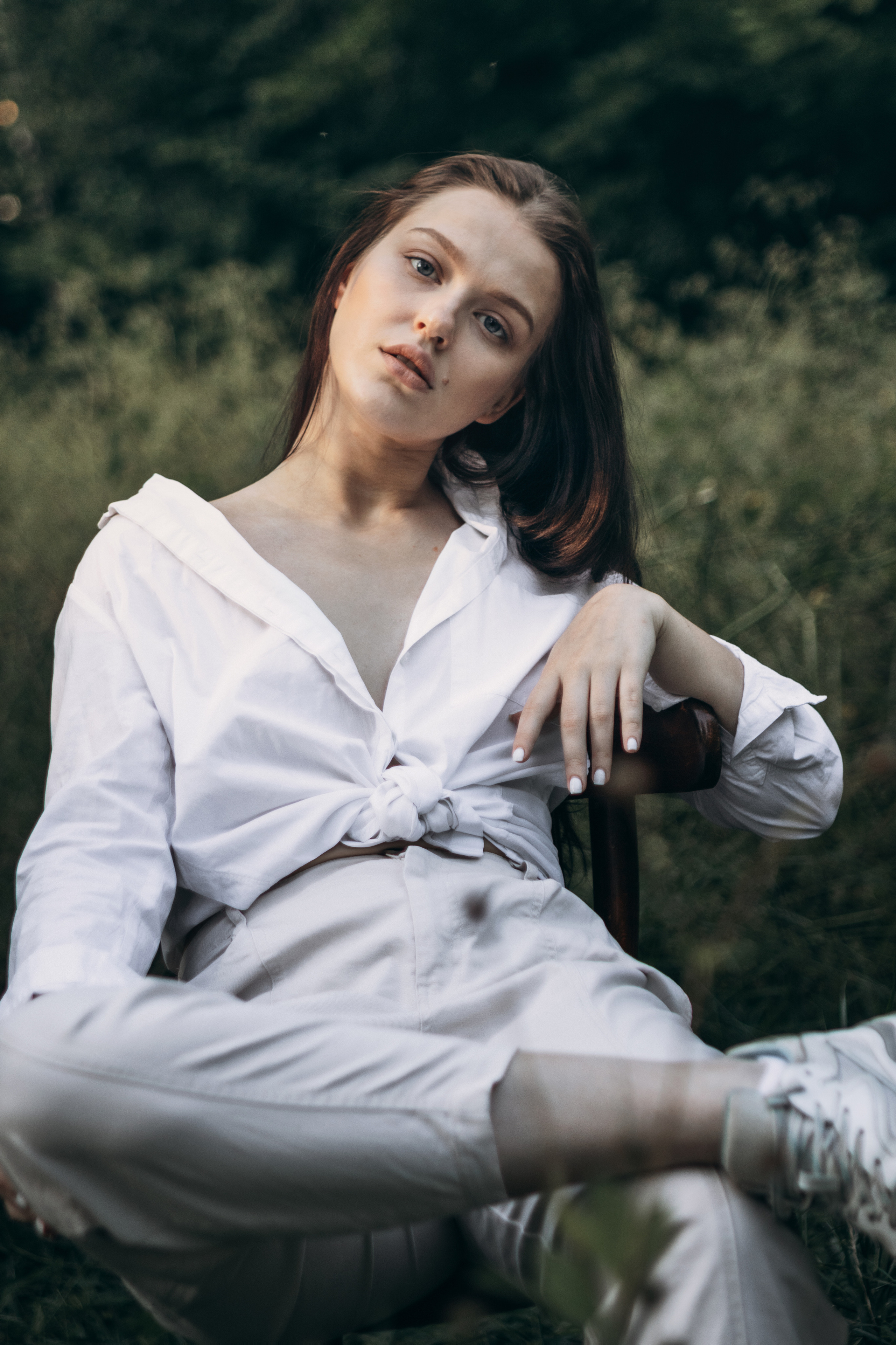 Девушка сидит на стуле в белой одежде на фоне леса