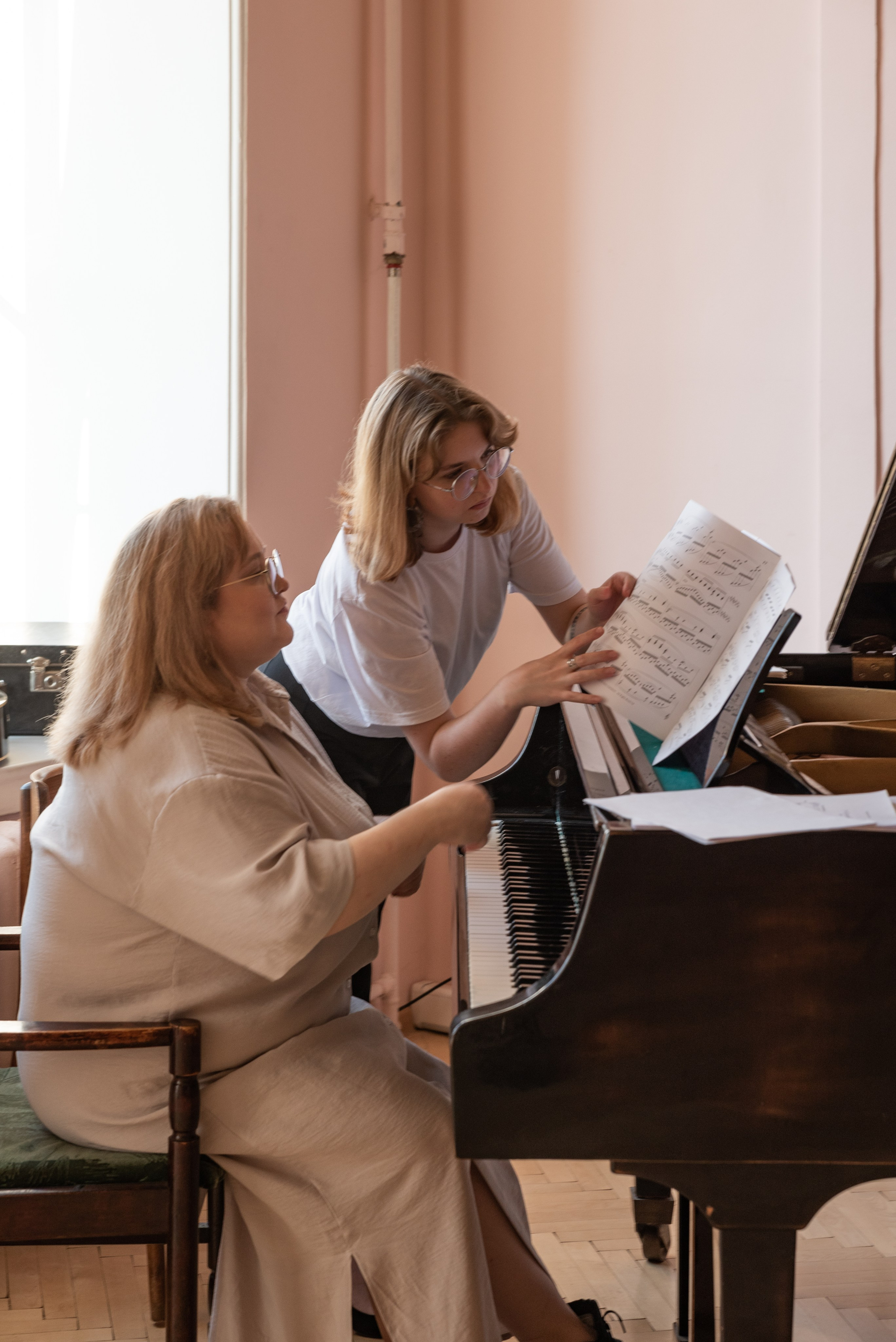 Денщина сидит за роялем, девушка стоит рядом и перелистывает ноты.