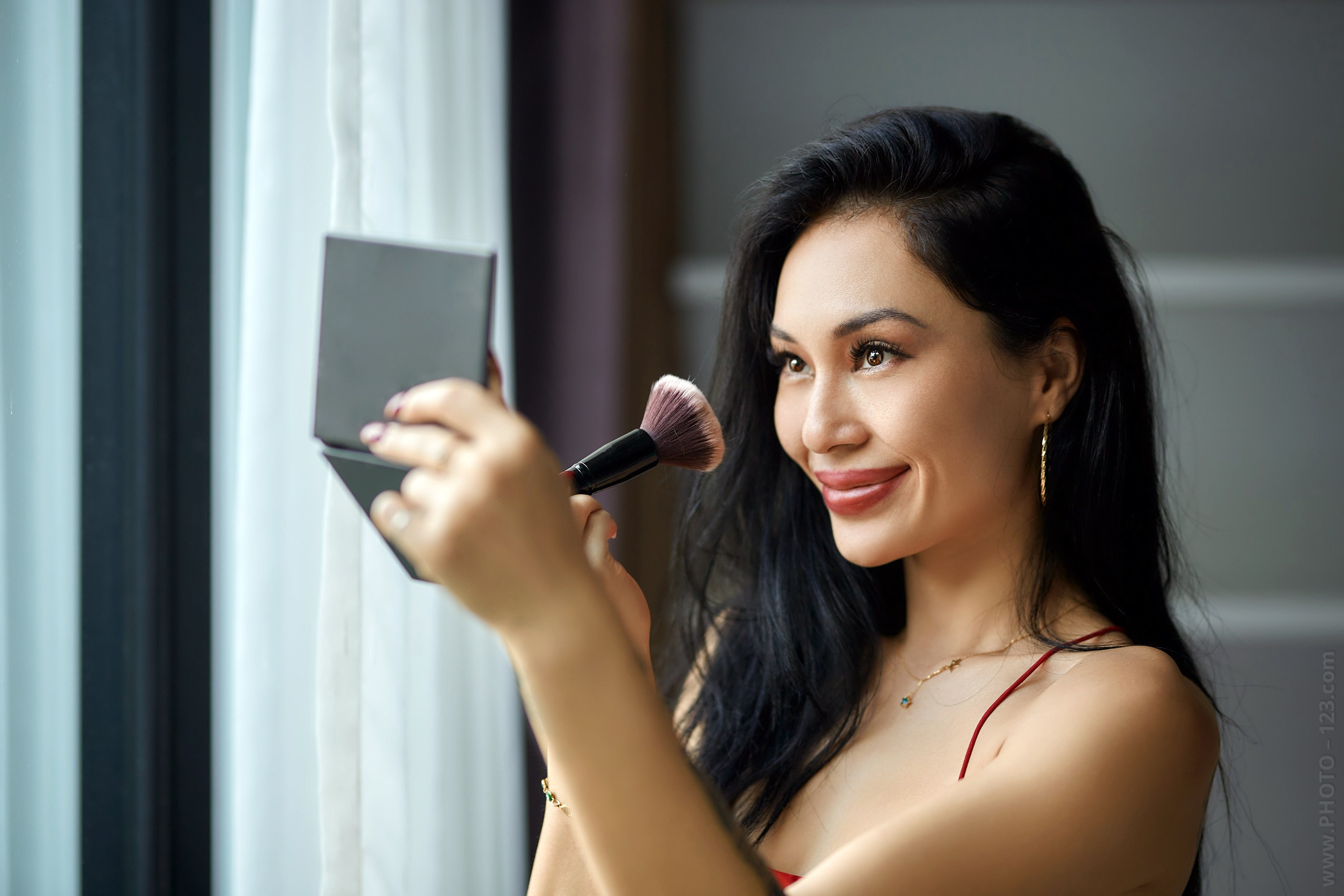 Beauty portrait of a woman applying makeup by a window in natural light, intimate lifestyle photography by a commercial photographer in Phu Quoc, Vietnam