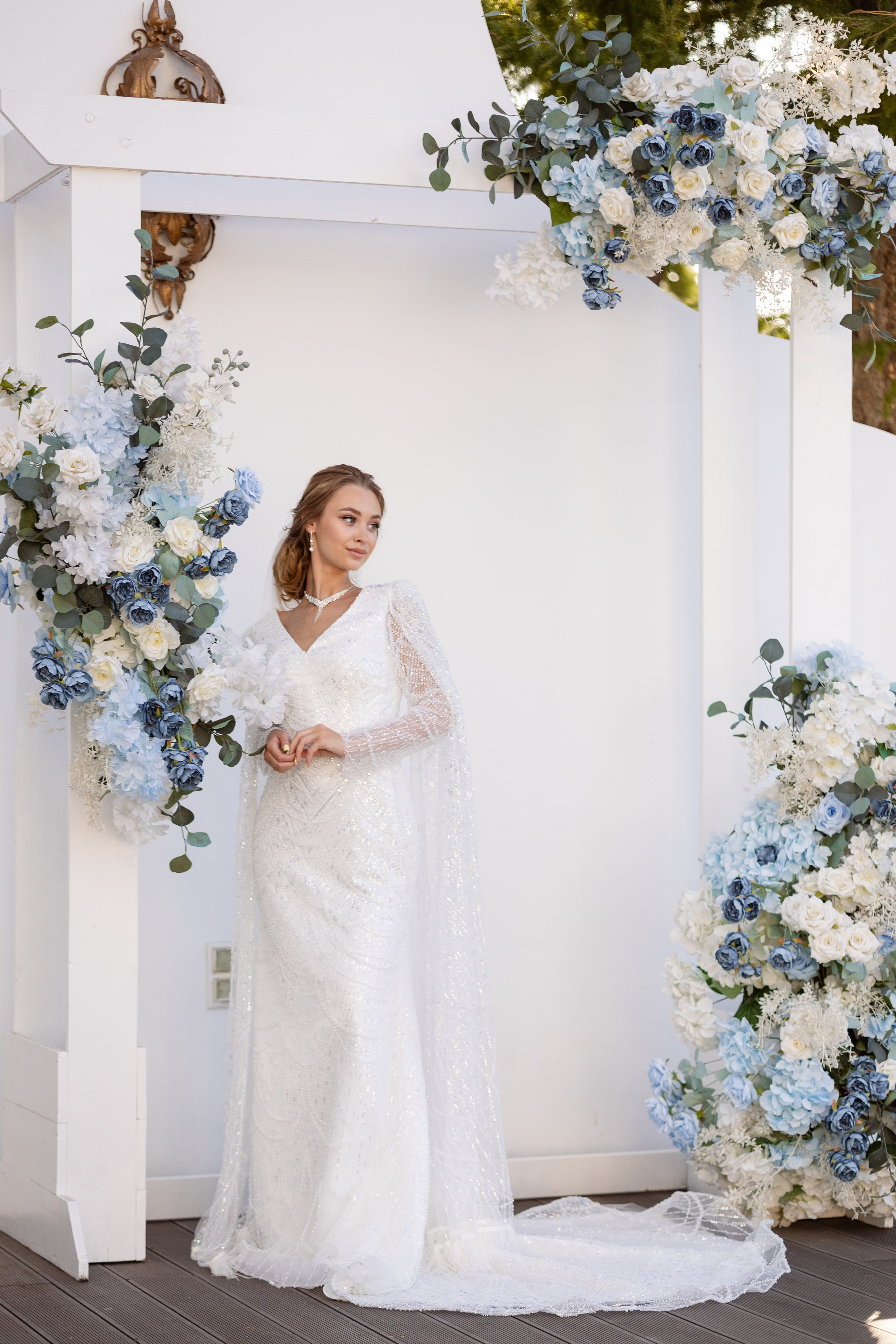 Невеста у белой стены, украшенной цветами.