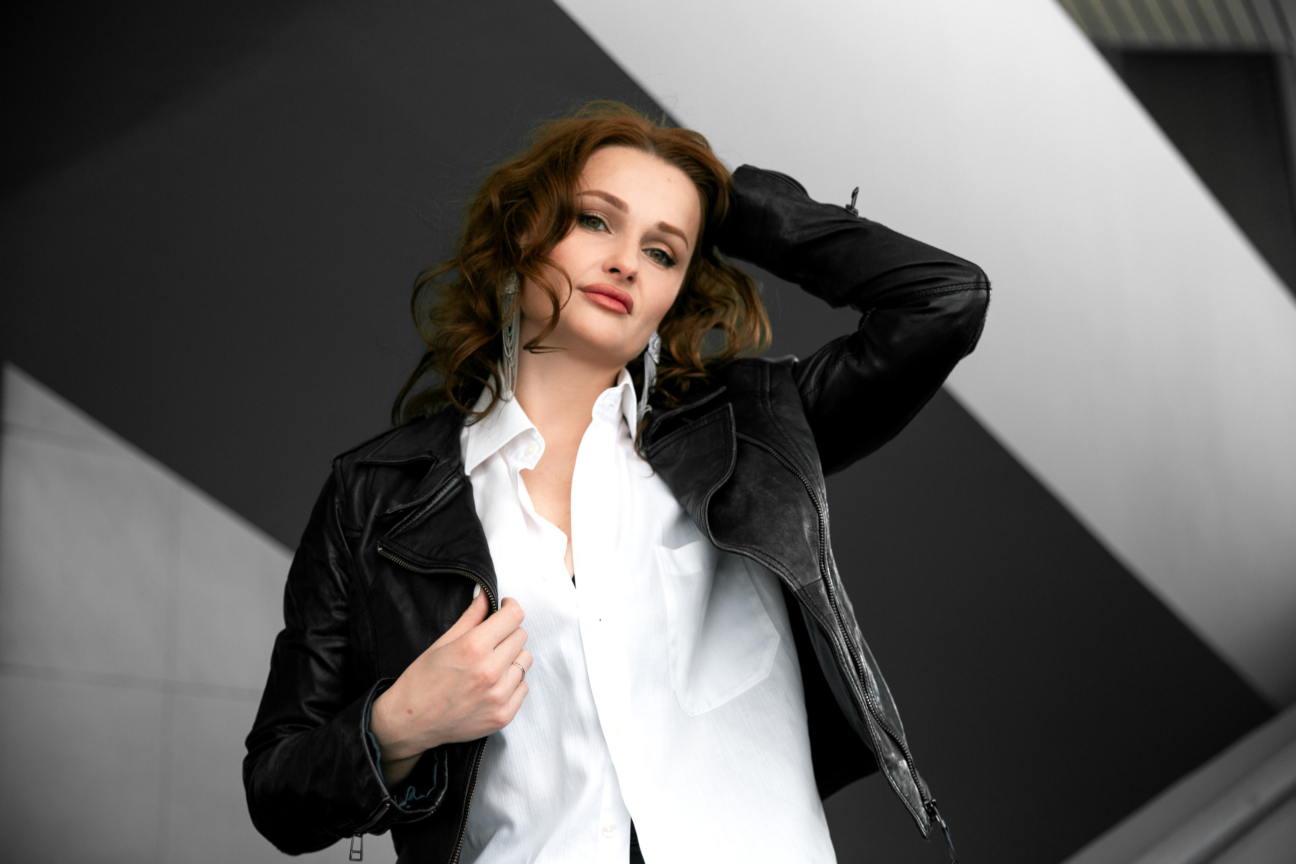 a photo of a red-haired girl in a black jacket against the background of a building