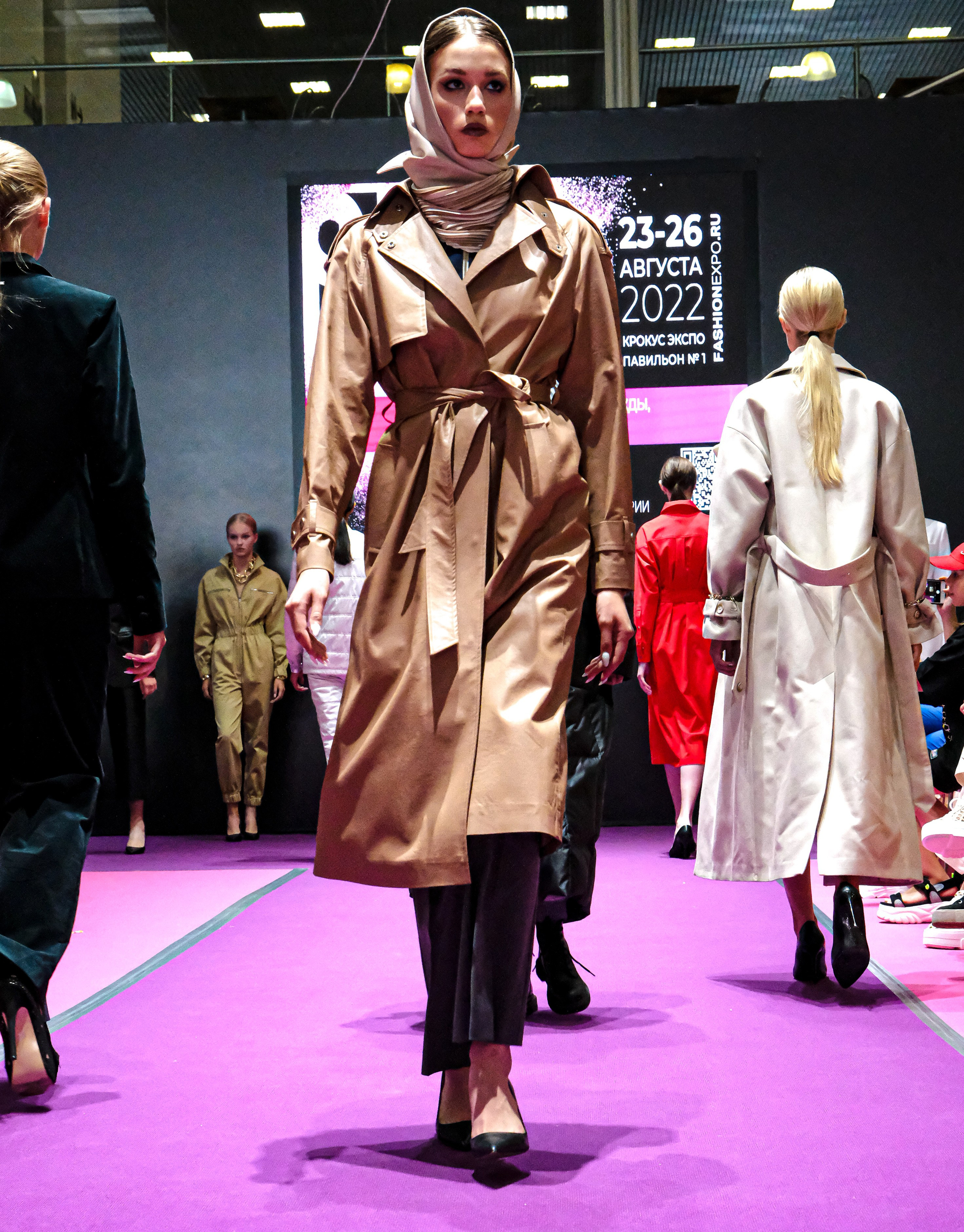  "Модели в ярких нарядах проходят по подиуму во время показа мод, освещенные яркими софитами и окруженные восторженными зрителями."