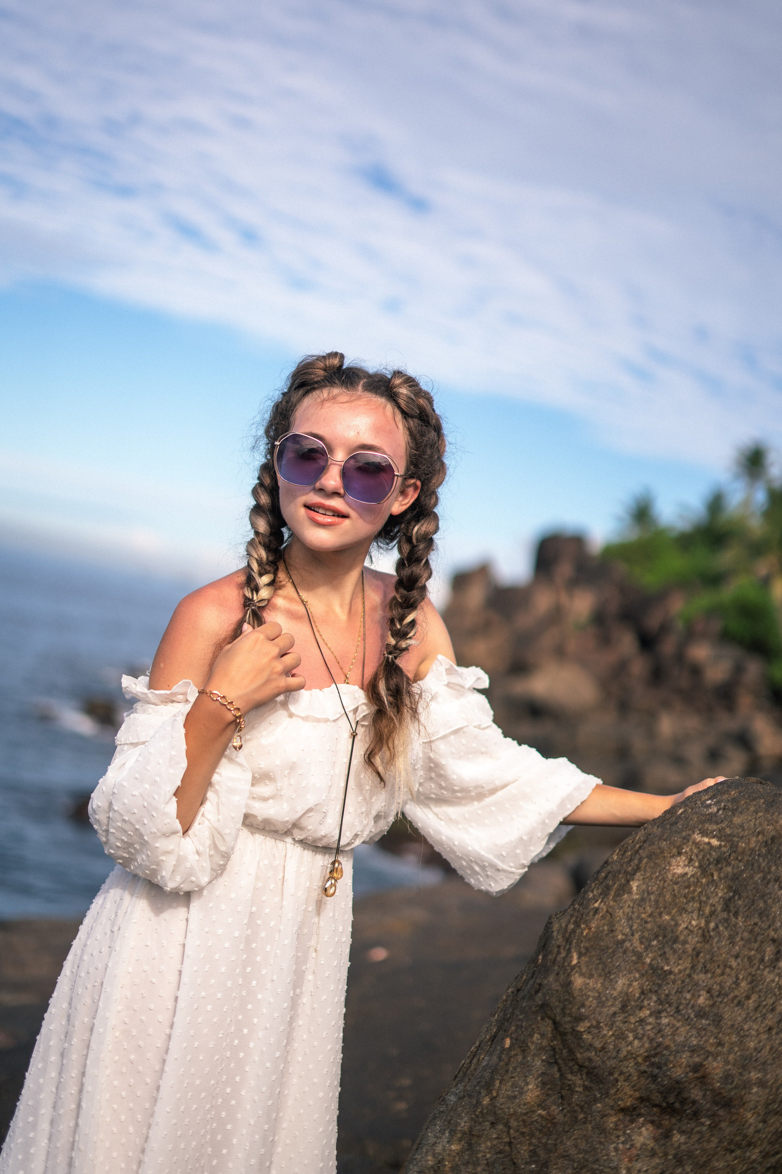 a girl in a white dress and glasses taking stylish shots on the rocks